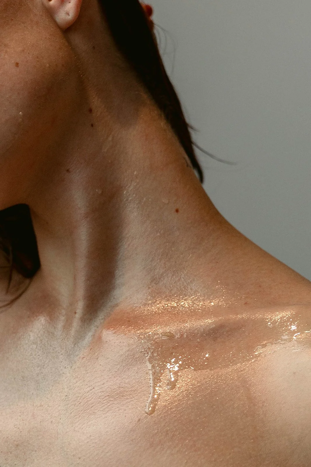 A close-up photograph of woman's neck glistening with water and skincare products.