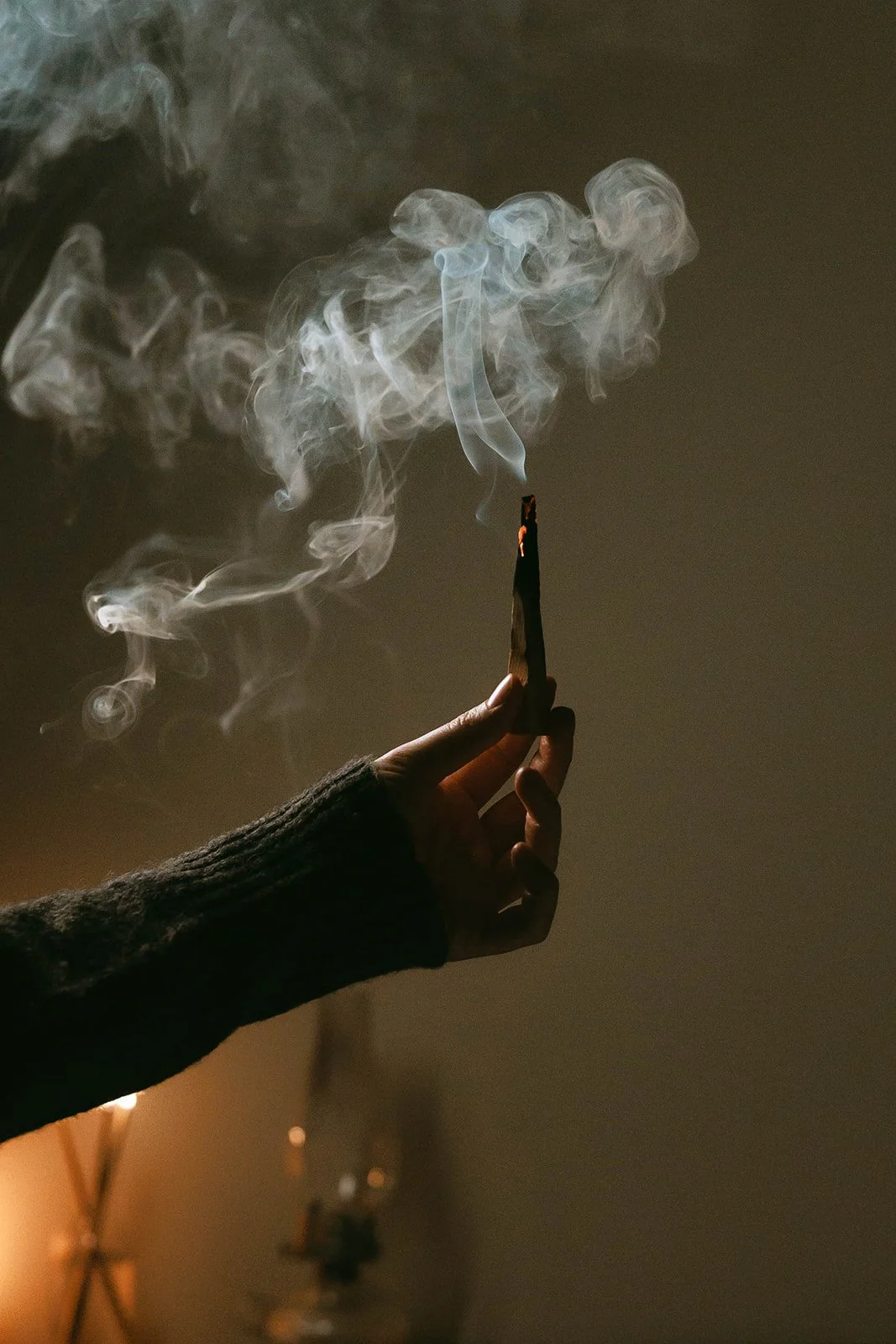 A person holding a lit palo santo incense with smoke rising in a dimly lit and serene room.