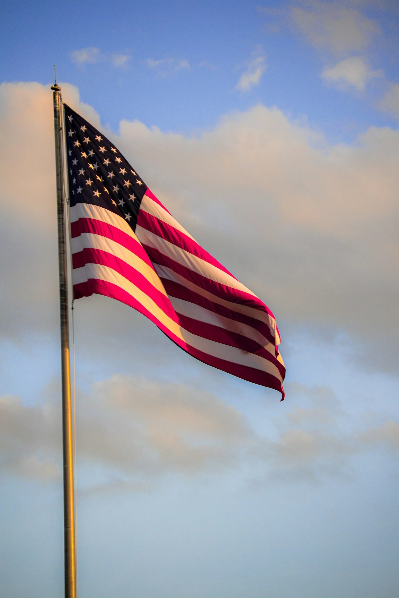 American flag waving against a sky with clouds during sunset.