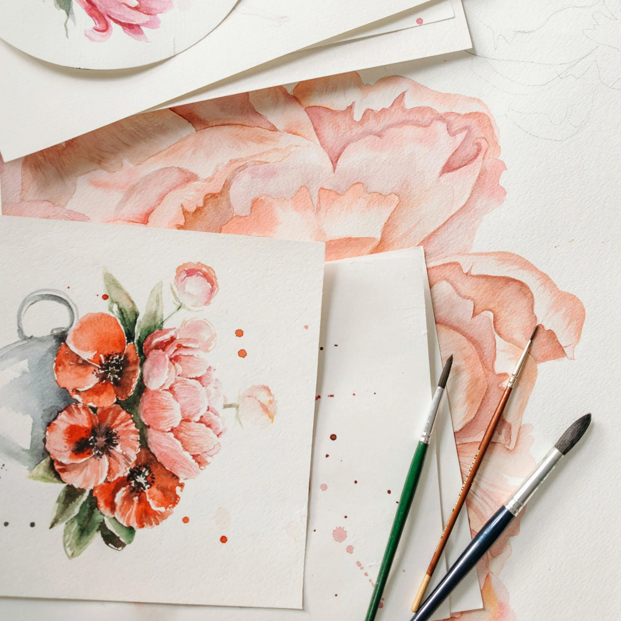 Watercolor floral paintings of pink and orange flowers on textured paper with watercolor brushes nearby.