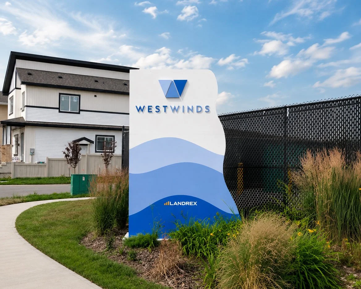 A large white sign with blue design elements and the text 'WESTWINDS' and 'LANREX' in front of a residential building with a sidewalk and landscaped grass and plants.