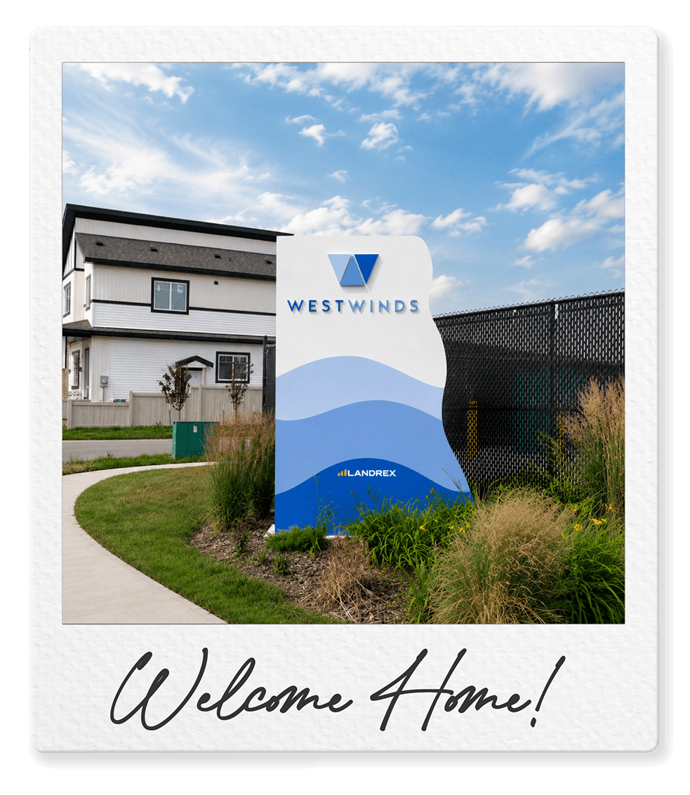 Photo of a sign for Westwinds, located near a sidewalk and a grassy area, with a house and a fence in the background under a partly cloudy sky. The sign features abstract blue wave designs and the words 'Westwinds' and 'Landrex'. The photo has a white border with the handwritten phrase "Welcome Home!" at the bottom.