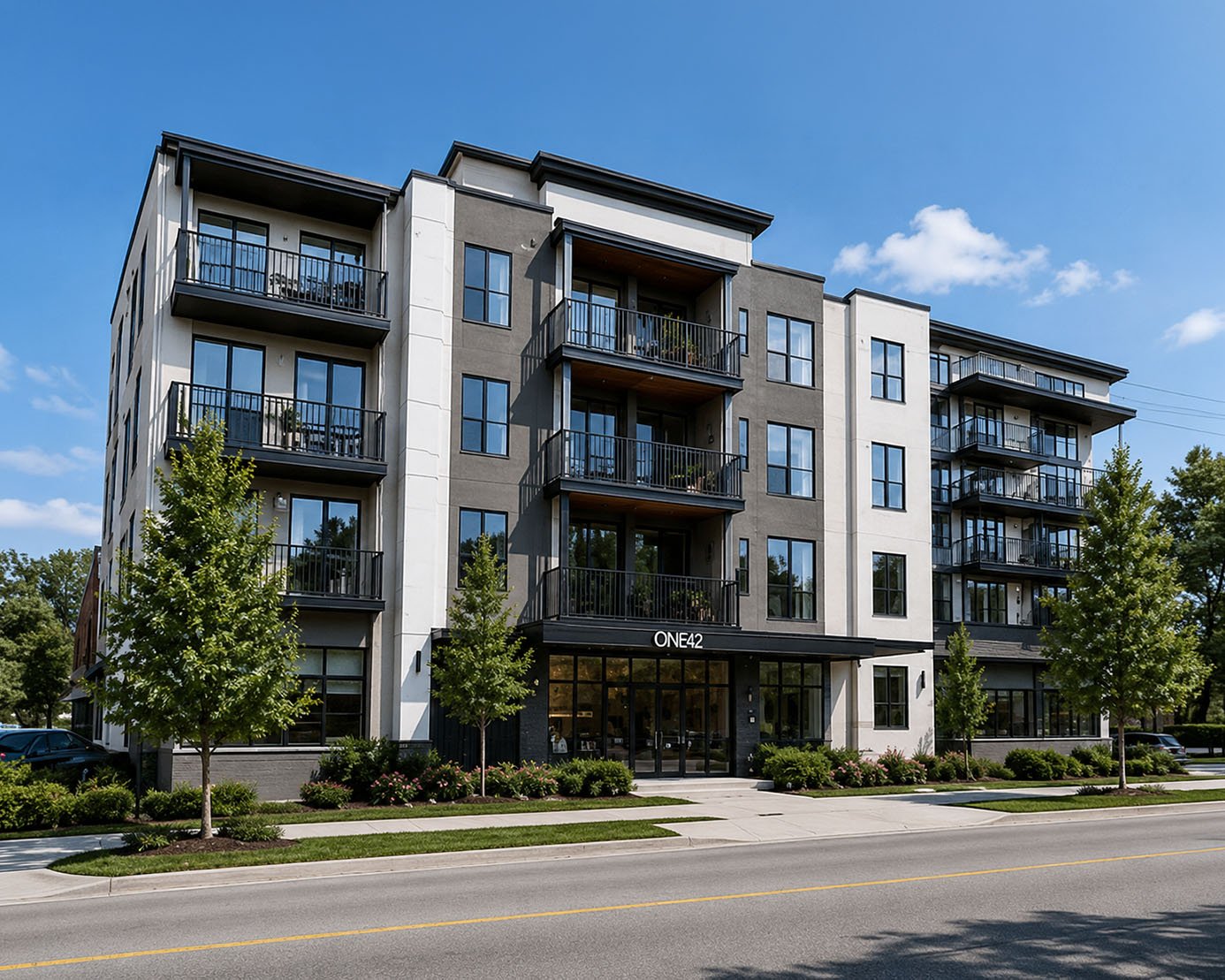 Modern multi-story apartment building with balconies, surrounded by trees and a sidewalk, under a clear blue sky.