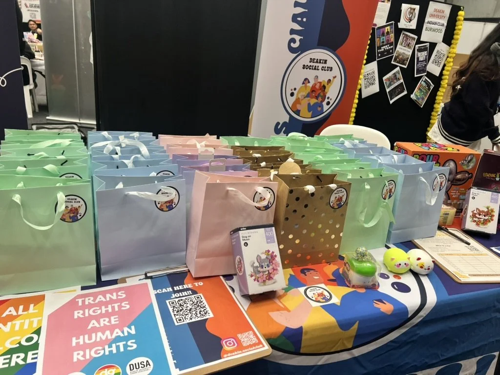 Table with colorful gift bags, toys and informational materials at a Deakin Social Club event.