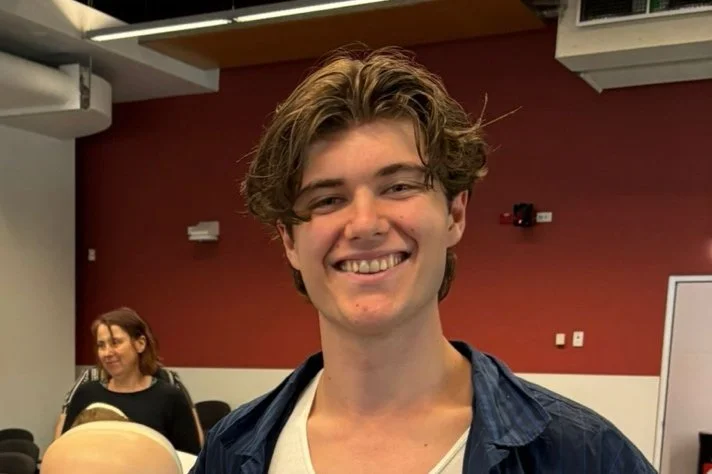 Young man (President) with wavy brown hair smiling in a classroom