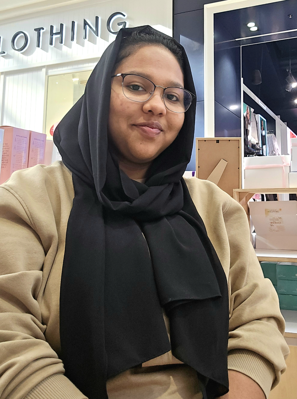 A woman with glasses and a black headscarf (Sponsorship Officer) sitting down and smiling at the camera.