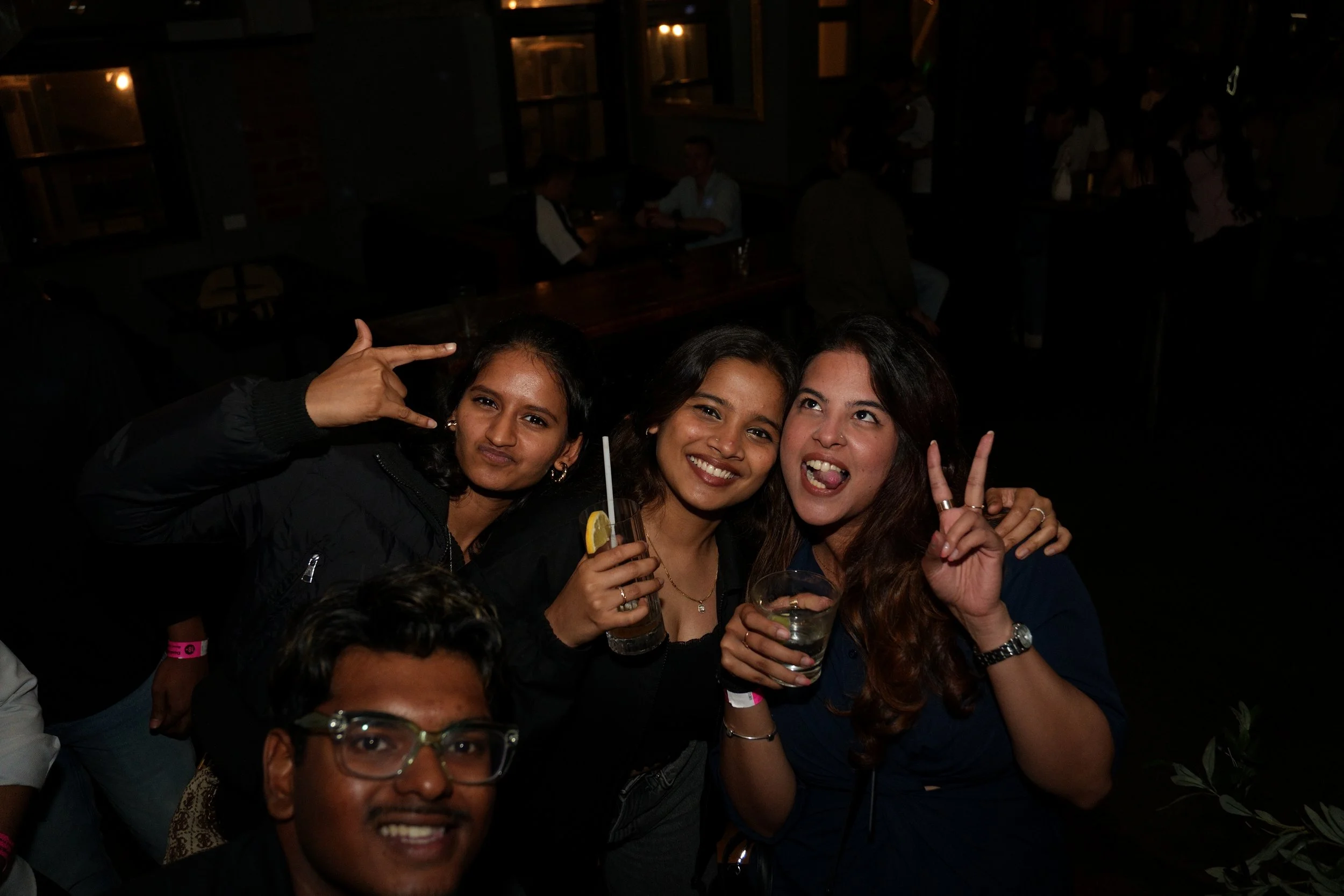 Three women and one man smiling and making peace signs, enjoying drinks at our 2026 Barhop event