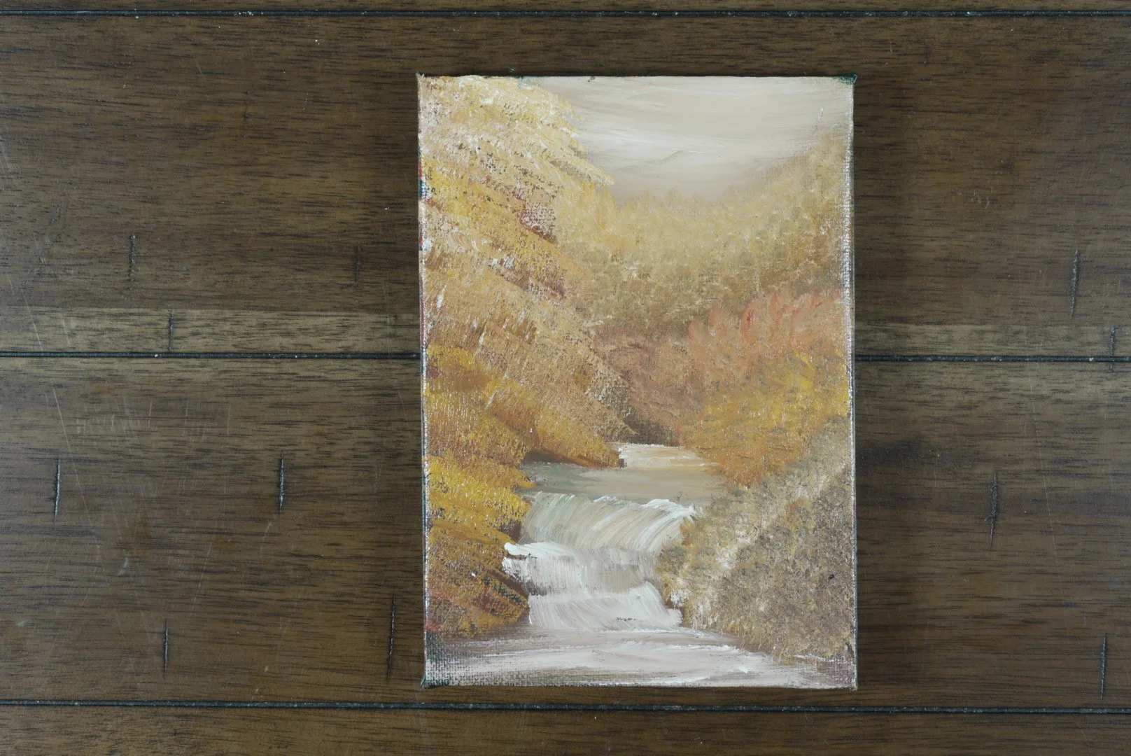 Unframed 5x7 canvas of an autumn waterfall, shown on a wood floor