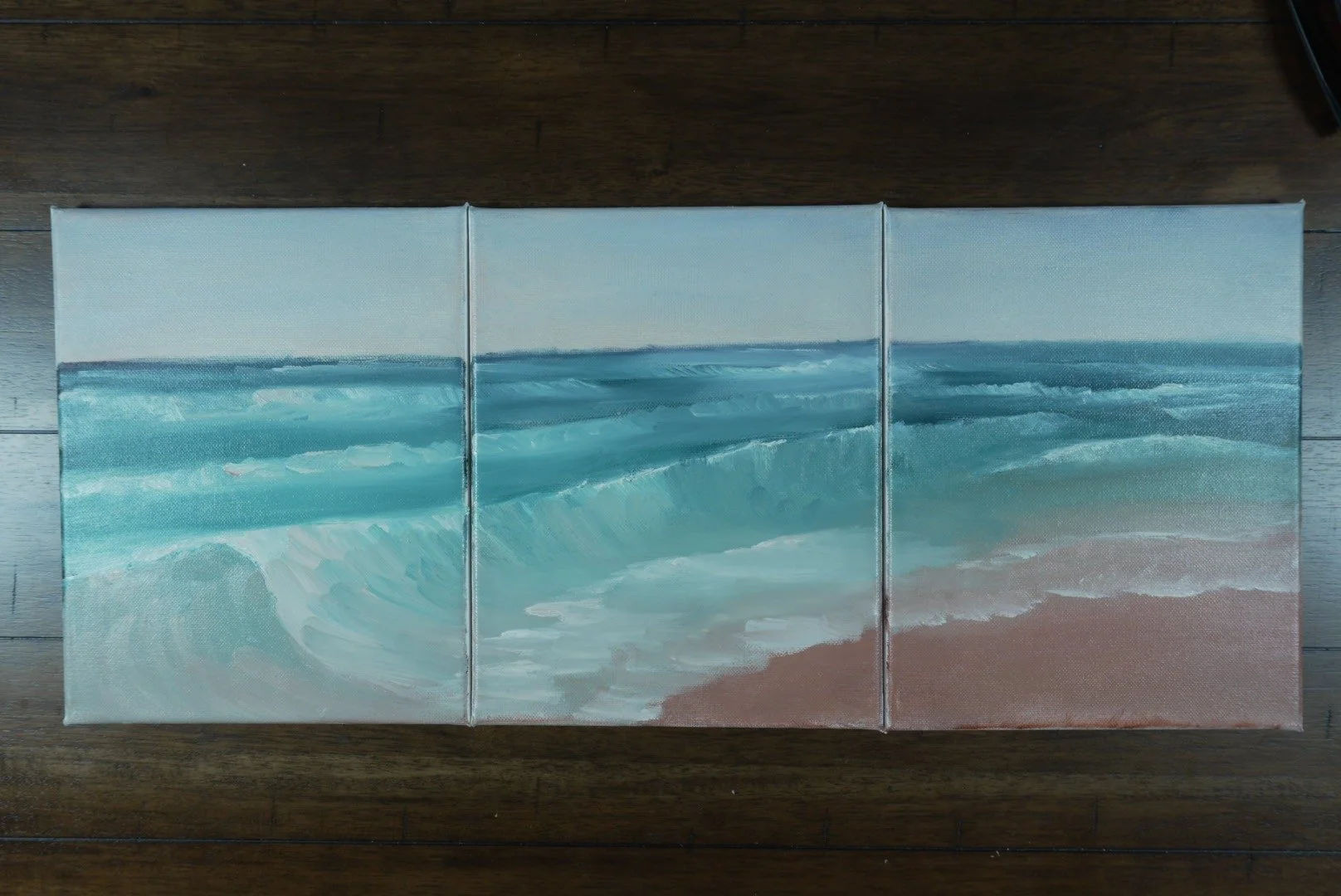 Three small unframed canvases of the Jersey Shore surf laid side by side on a wood floor