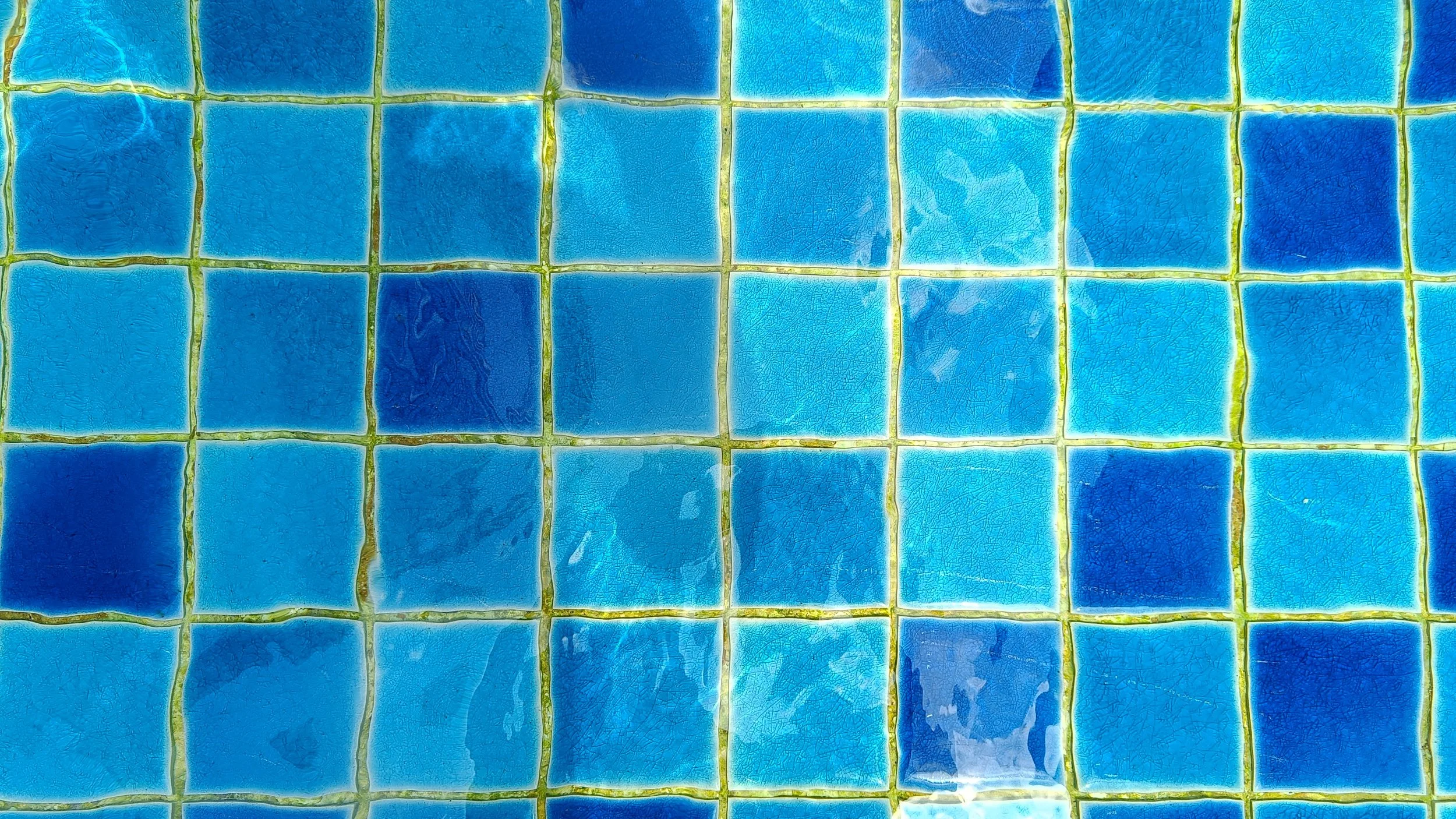 Close-up view of a mosaic of blue ceramic tiles with yellow grout lines.