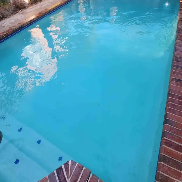 An outdoor swimming pool with blue water, brick edge, and steps leading into the pool.