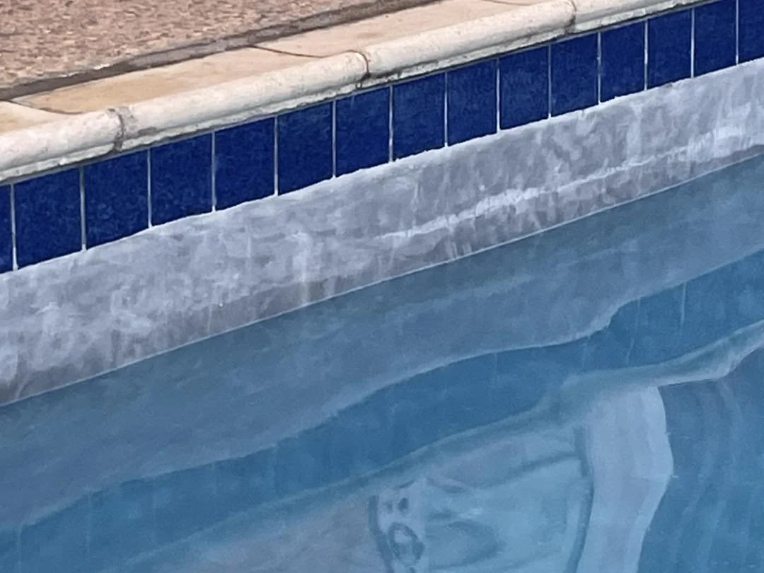 Close-up of a swimming pool edge with blue tiles and a pool skimmer in the water.
