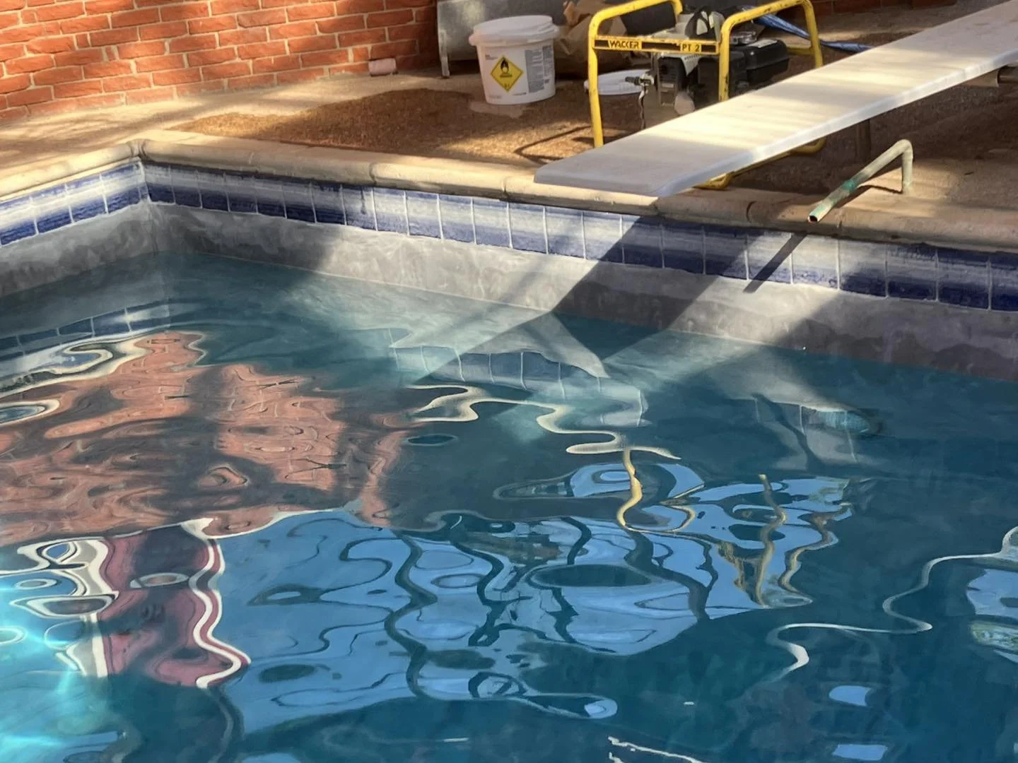 In-ground swimming pool with blue tiles and a built-in steps, surrounded by a concrete deck. Construction equipment and supplies are visible around the pool, indicating ongoing repairs or construction.
