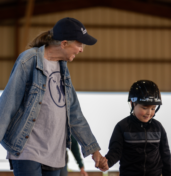An older woman and a young boy in a roller skating rink, holding hands.