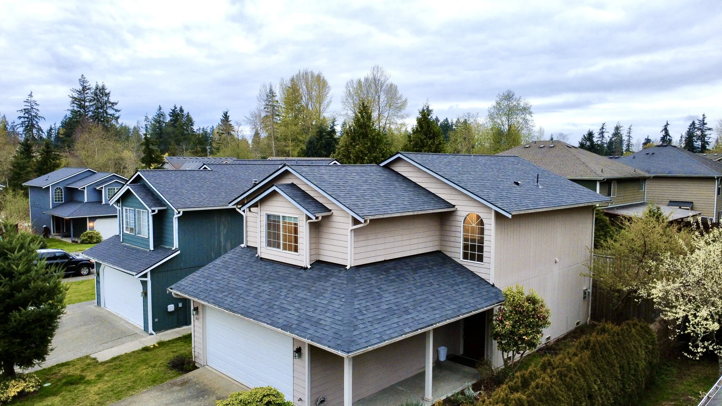 Aerial view of a row of modern suburban houses with well-maintained yards and trees in the background.