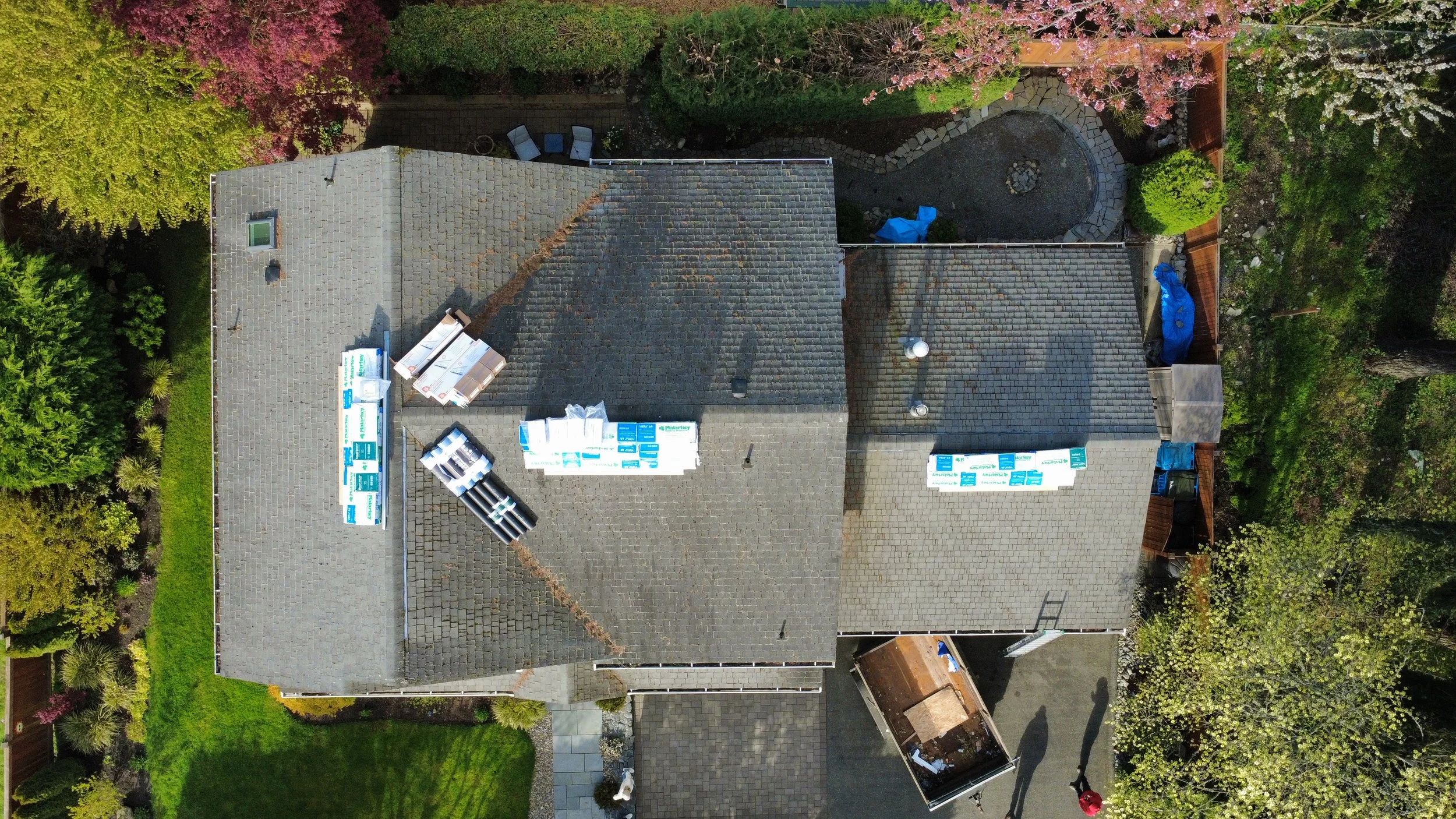 An aerial view of a house roof with ongoing roofing projects, construction materials, and surrounding greenery and trees.