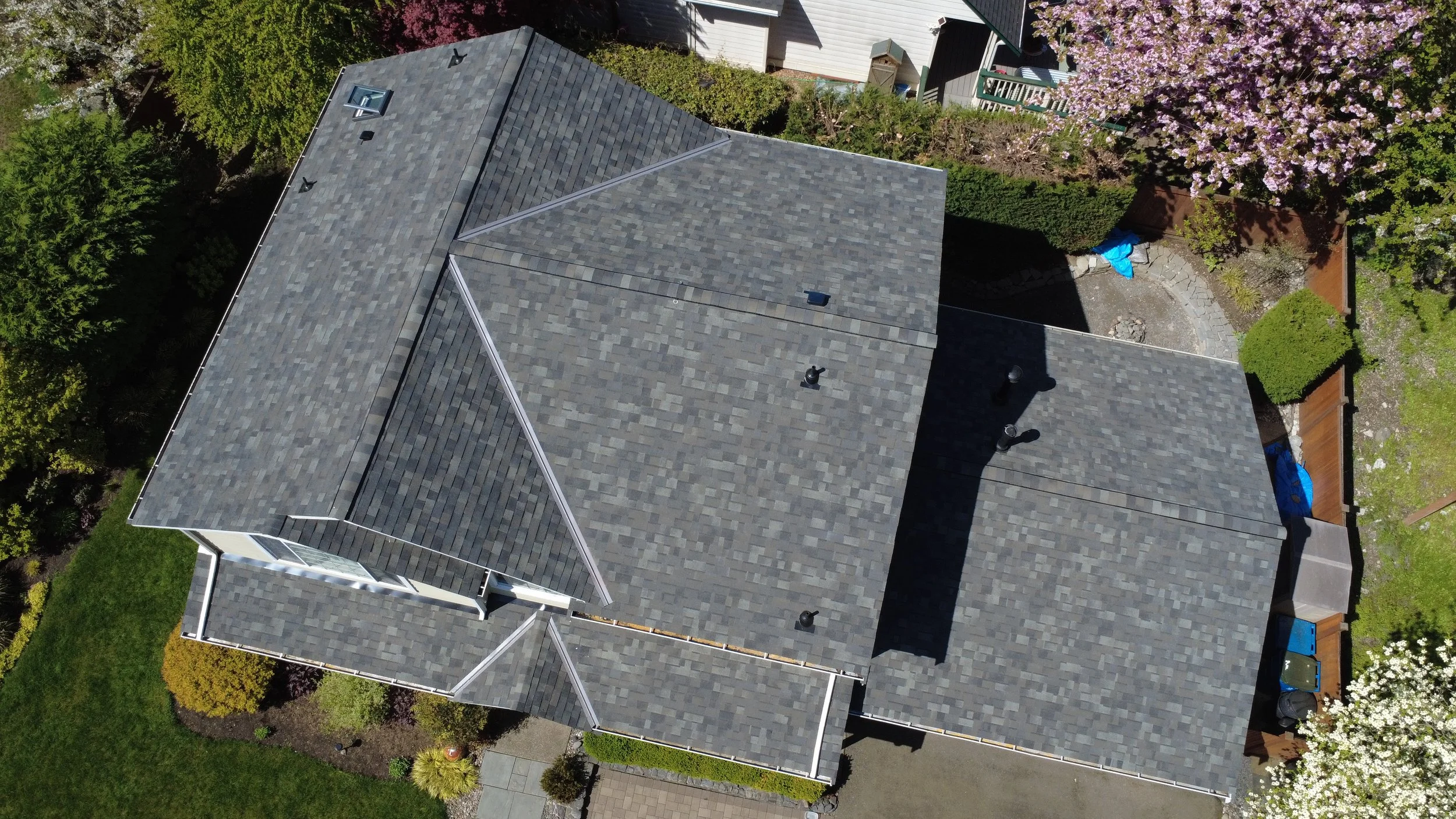Aerial view of a house with gray shingle roof, surrounded by trees and a backyard with landscaping.