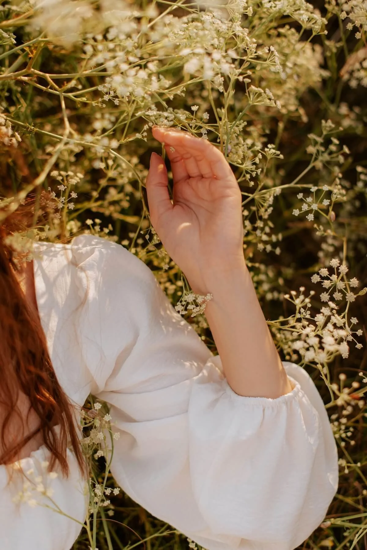 Woman in a white dress gently touching wildflowers in golden light, symbolising openness, presence and connection to self