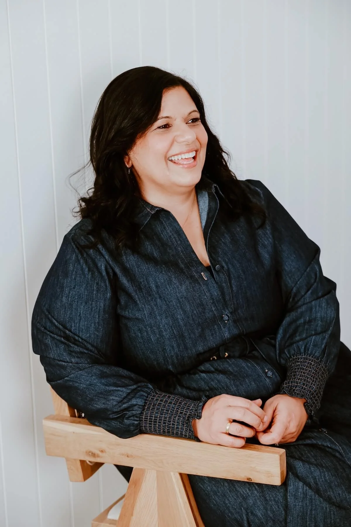 Alfina Lofaro, Brisbane relationship coach and kinesiologist, sitting on a timber chair smiling