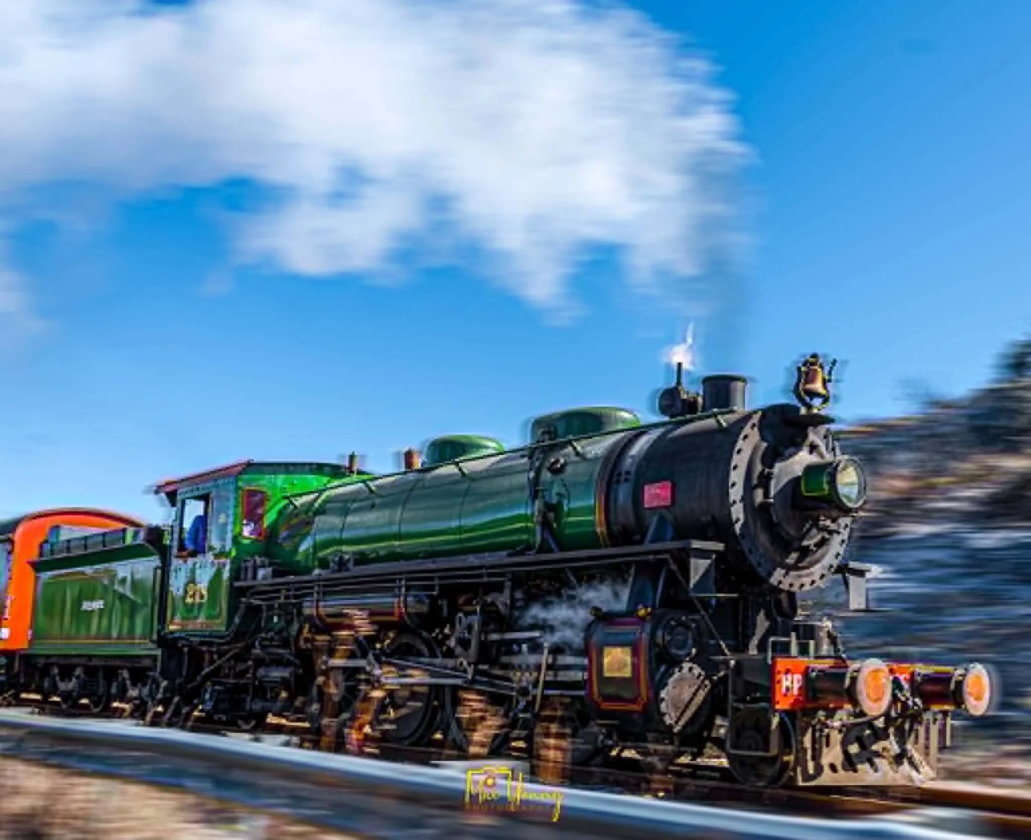 Motion-blurred image of a colorful train moving at high speed on a track against a blue sky with clouds.