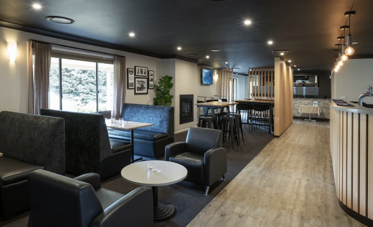 Interior of a modern lounge with black chairs, sofas, wall art, a window, a TV, and wooden dividers.