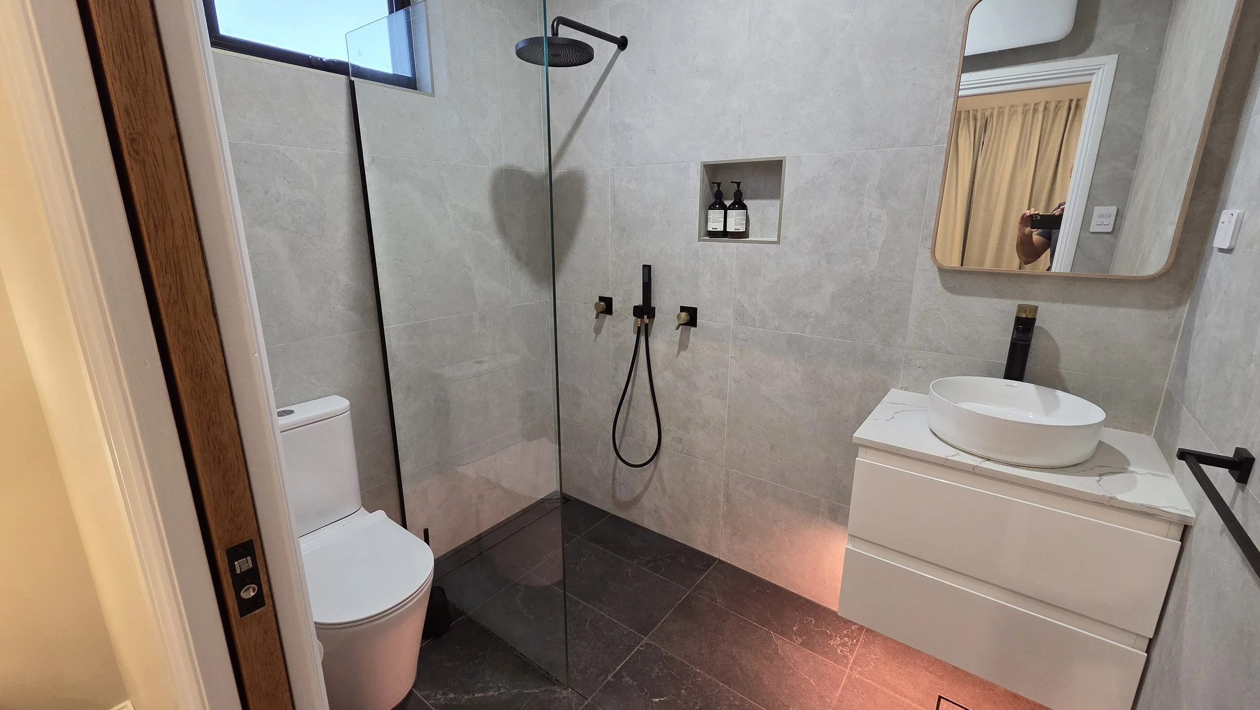 The ensuite bathroom features a rain shower and handheld shower, toilet, heater, exhaust fan, and ambient evening lighting beneath the vanity unit for a relaxing atmosphere.