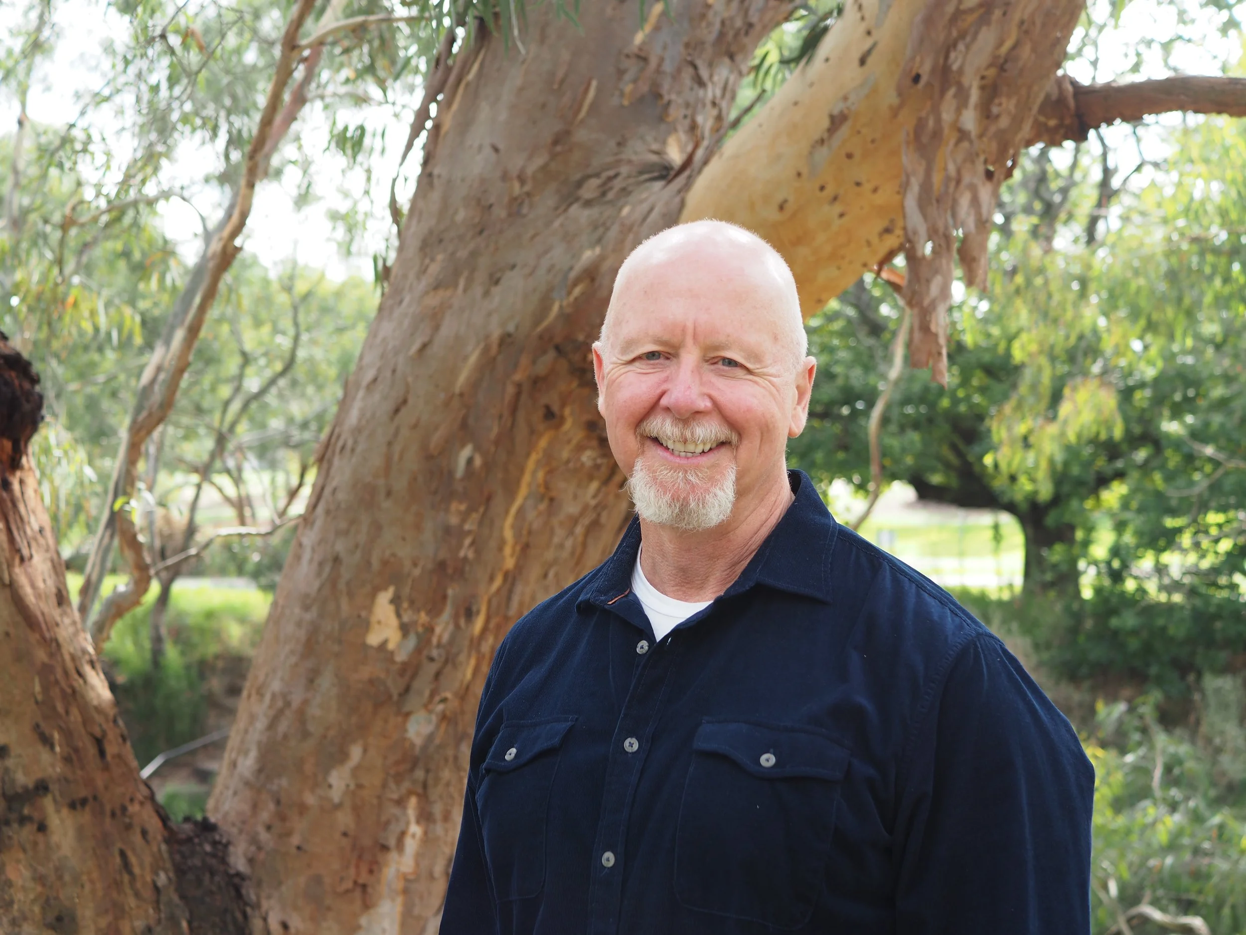 Brad Sadler, psychotherapist and counsellor, smiling and standing beside a large eucalyptus tree