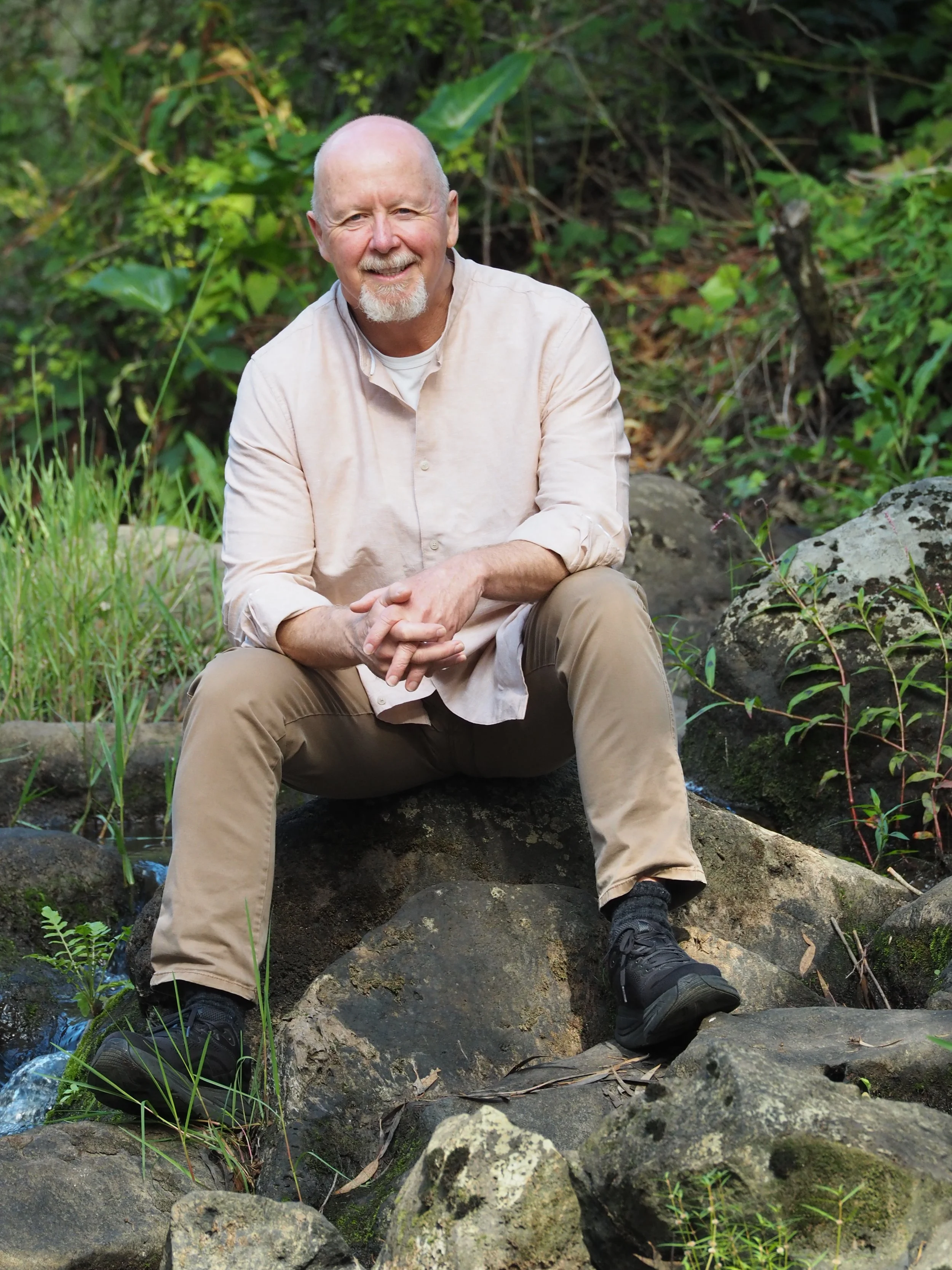 Brad Sadler, psychotherapist and counsellor, seated on rocks in a natural outdoor setting, smiling warmly at the camera