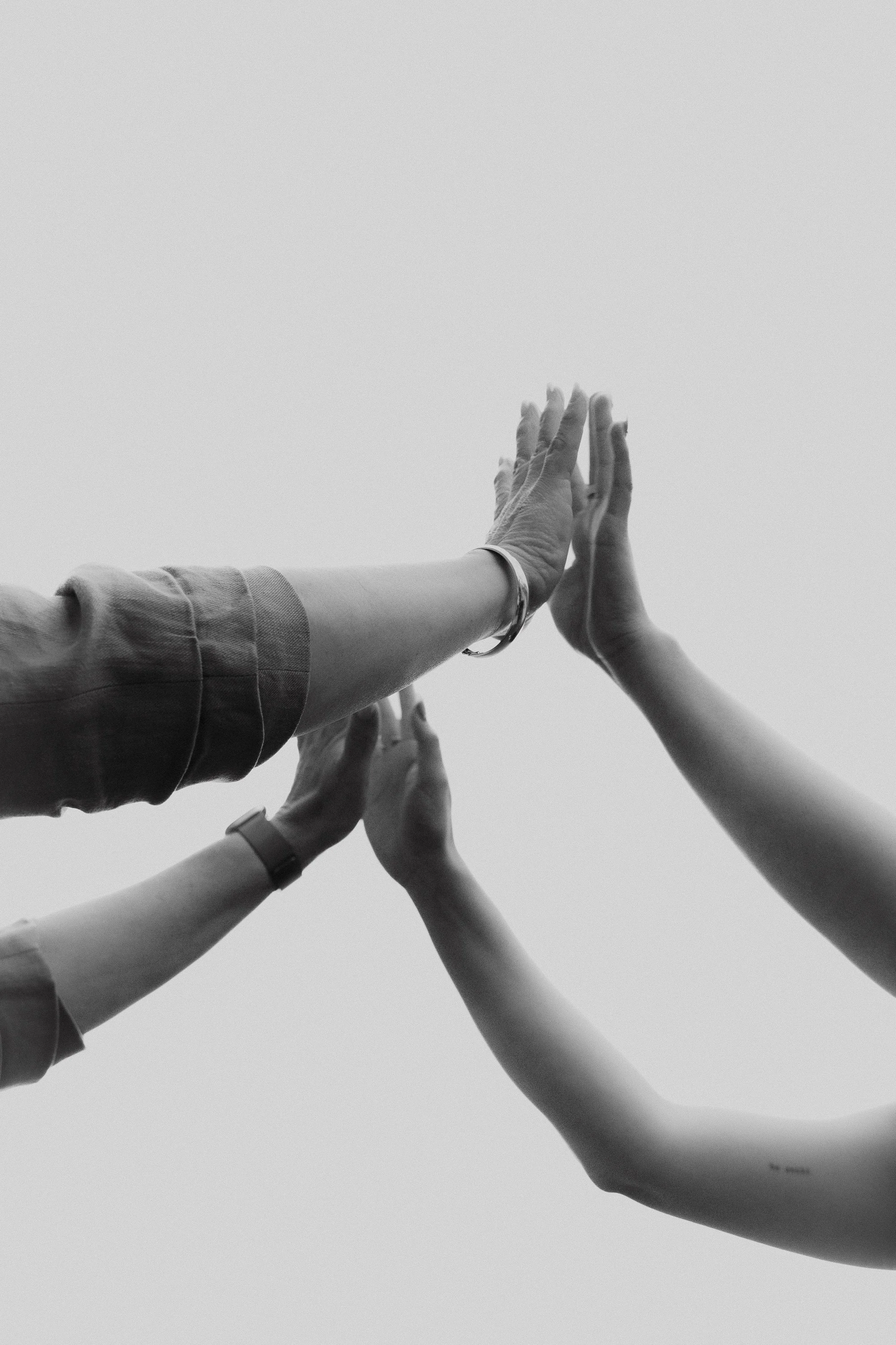 Multiple hands reaching out to touch in a high five, black and white photography.