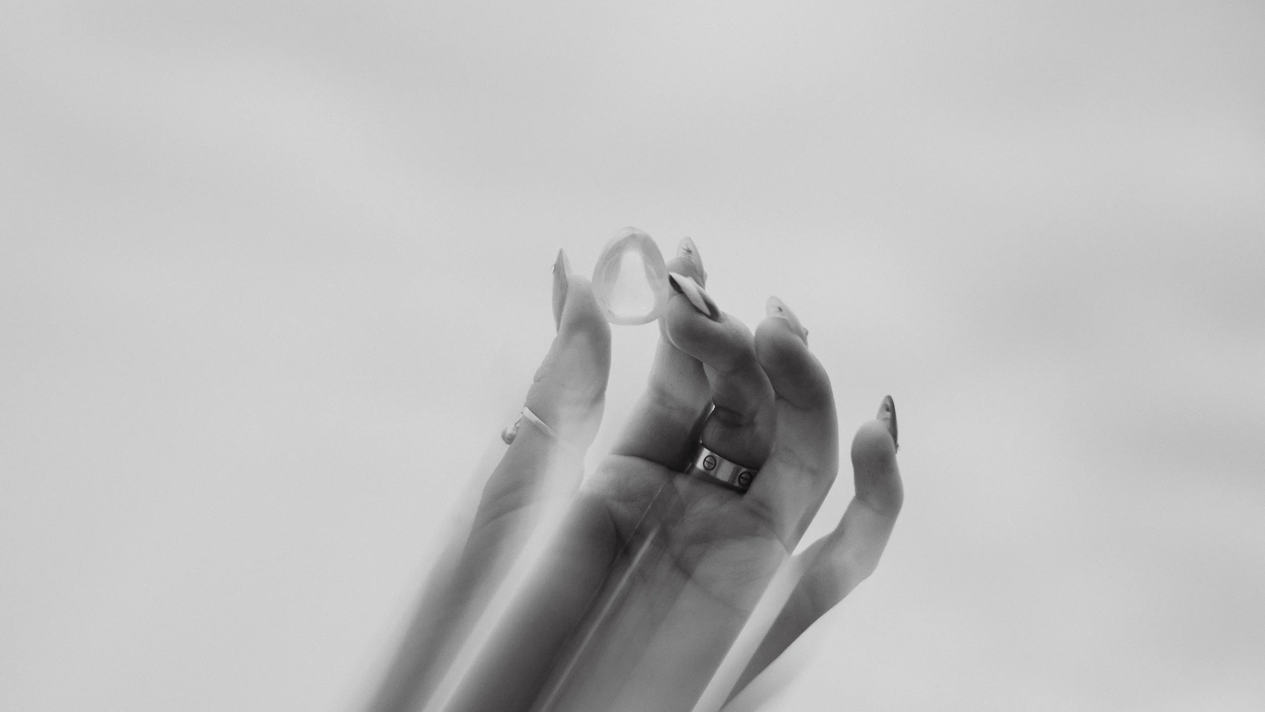 A hand holding a clear, oval-shaped gemstone or glass object against a plain, light background.