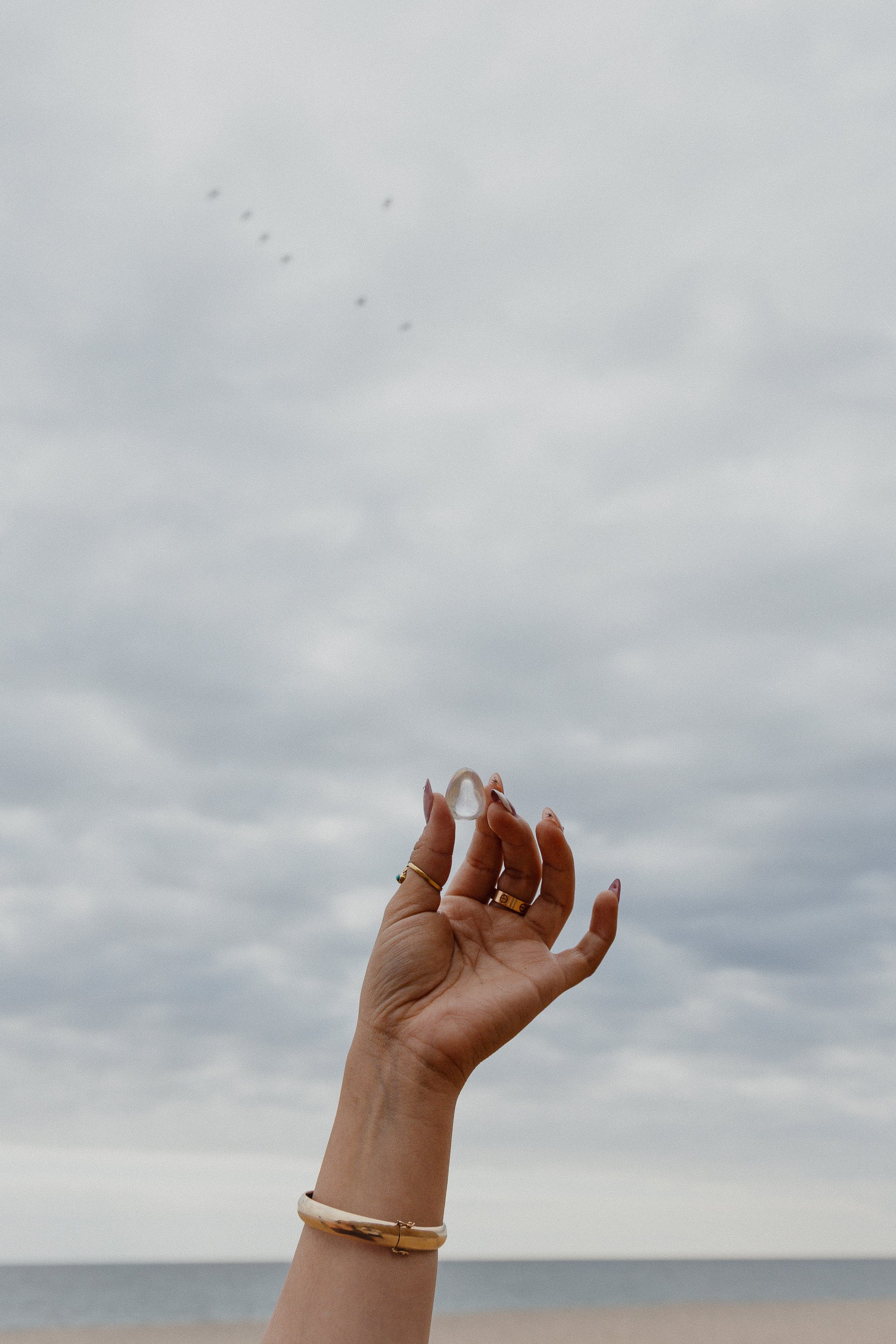 A person holding a small clear object with fingers extended, with a cloudy sky and distant ocean or lake in the background.