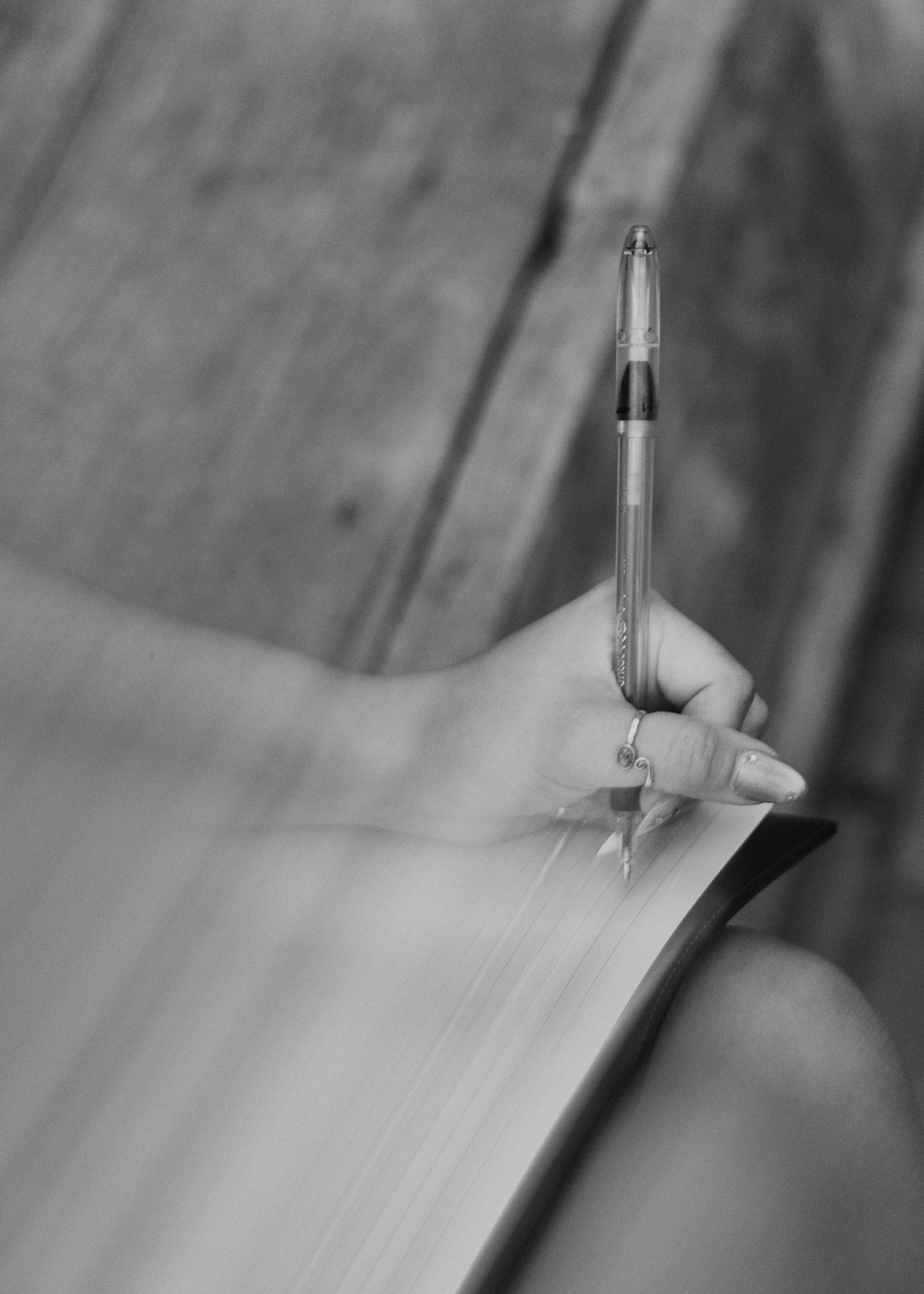 Close-up of a hand holding a pen, writing on a sheet of lined paper in an office or study setting.