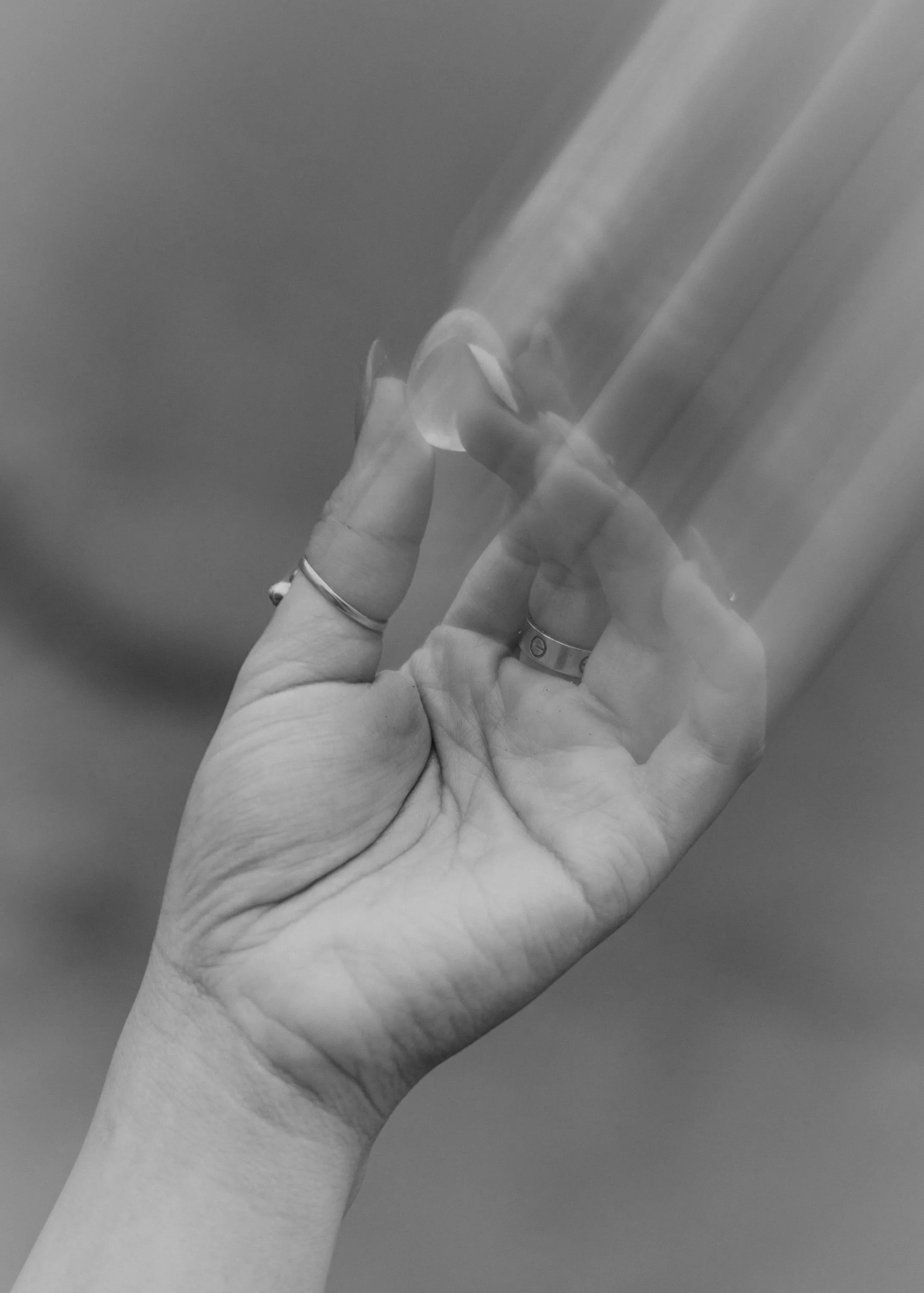 A hand with rings holding a transparent glass with a straw, taken from a low angle, in black and white.