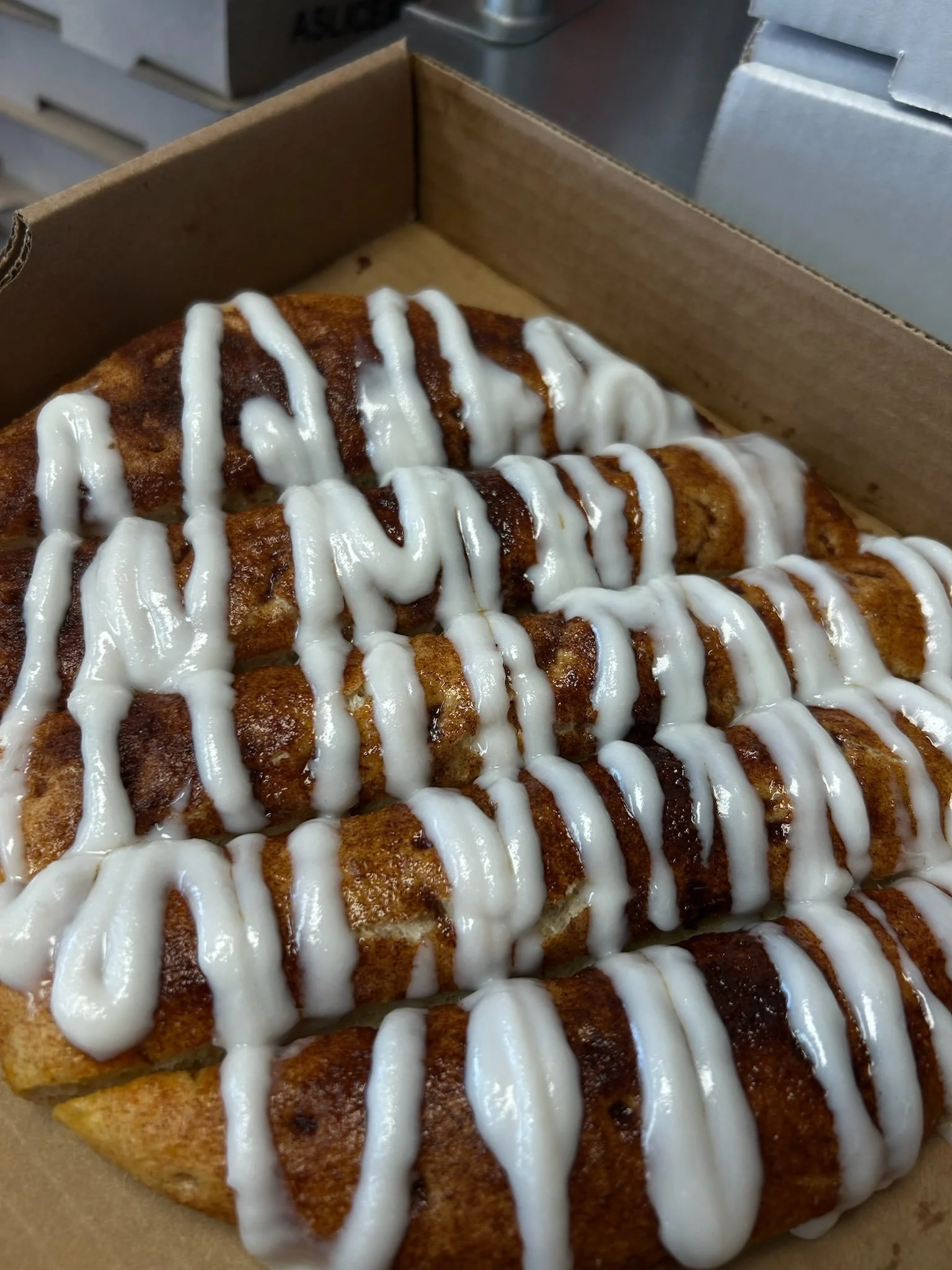 Two fried burritos with white drizzle sauce in a cardboard takeout box on a metal countertop.