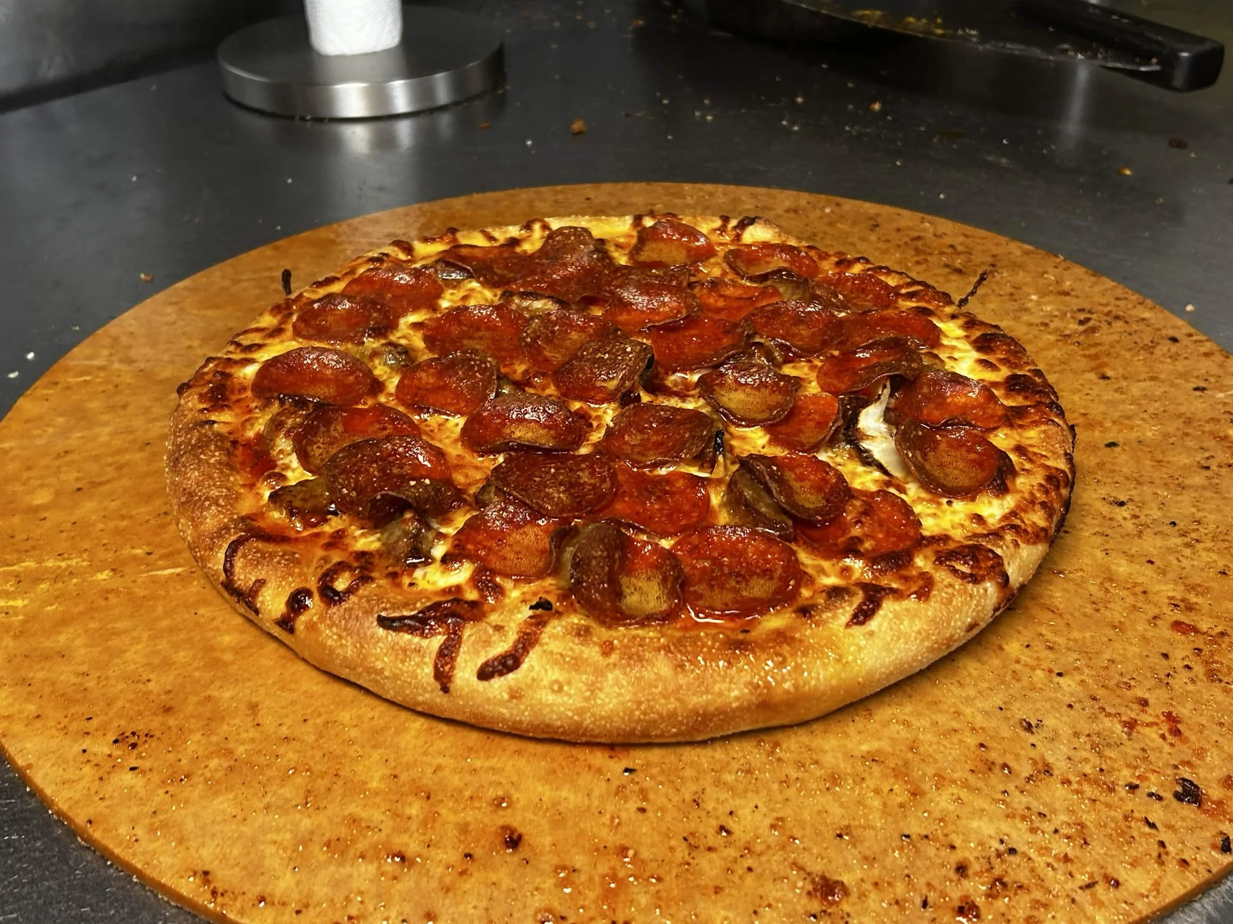 A freshly baked pepperoni pizza on a wooden pizza peel, with a black countertop in the background.