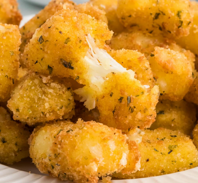 Close-up of golden-brown fried cauliflower bites with a crispy coating, one showing a bite revealing white cauliflower inside.