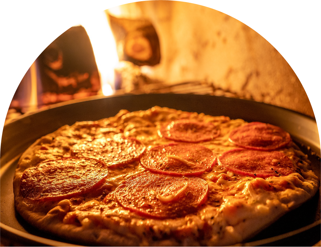 Pepperoni pizza baking in an oven with flames visible in the background.