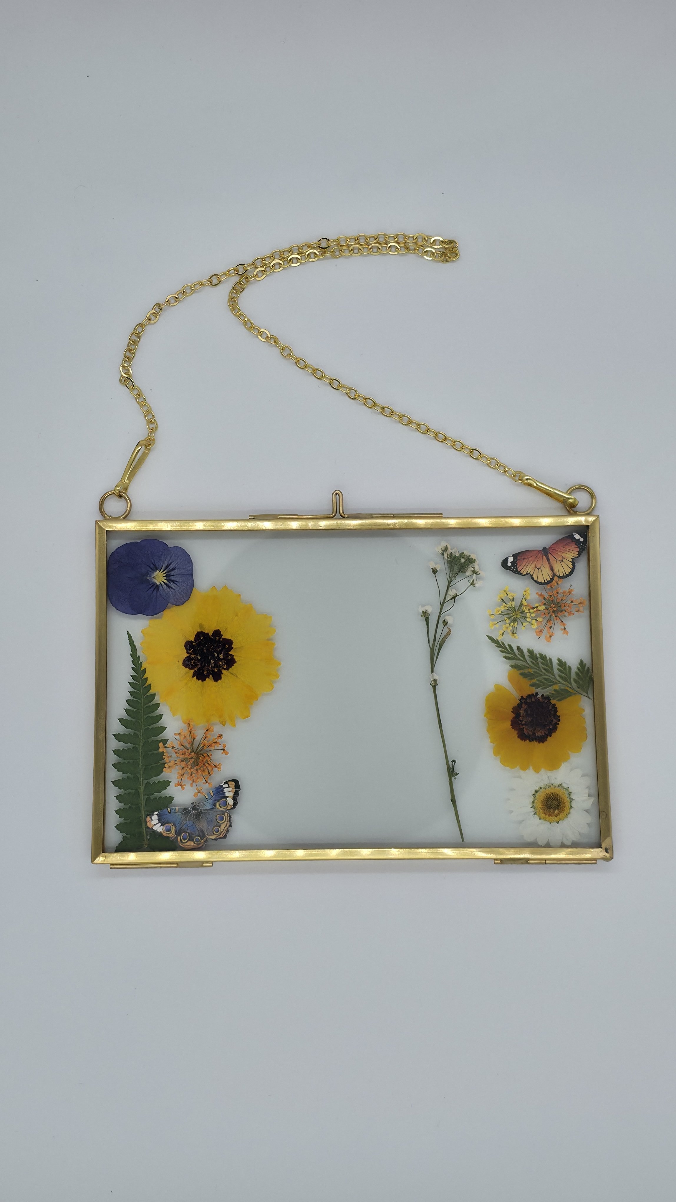 A picture of a gold-colored frame with flowers and butterflies inside, hanging by a gold chain.