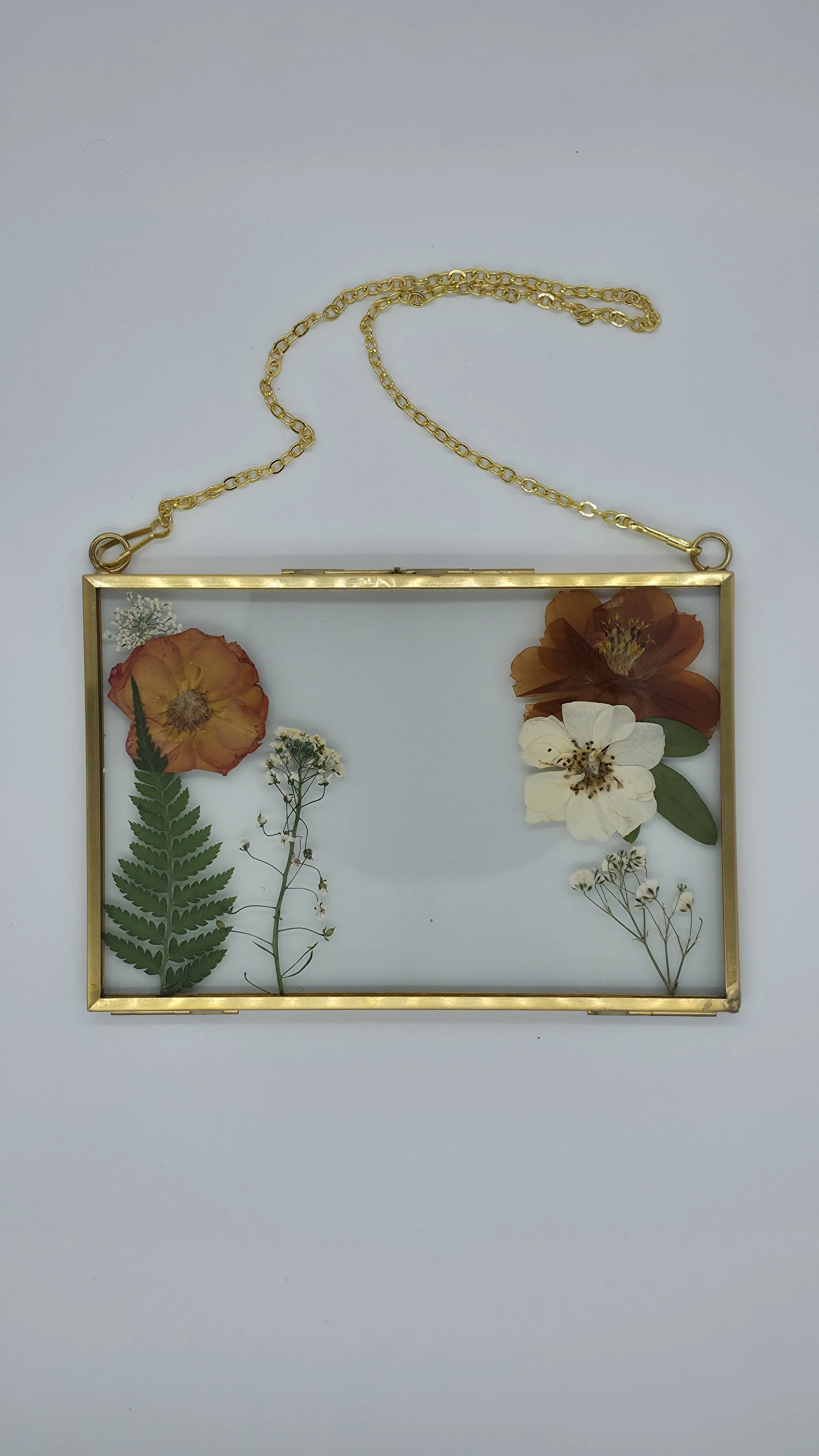 Gold frame with pressed flowers and leaves, hanging on a white background.