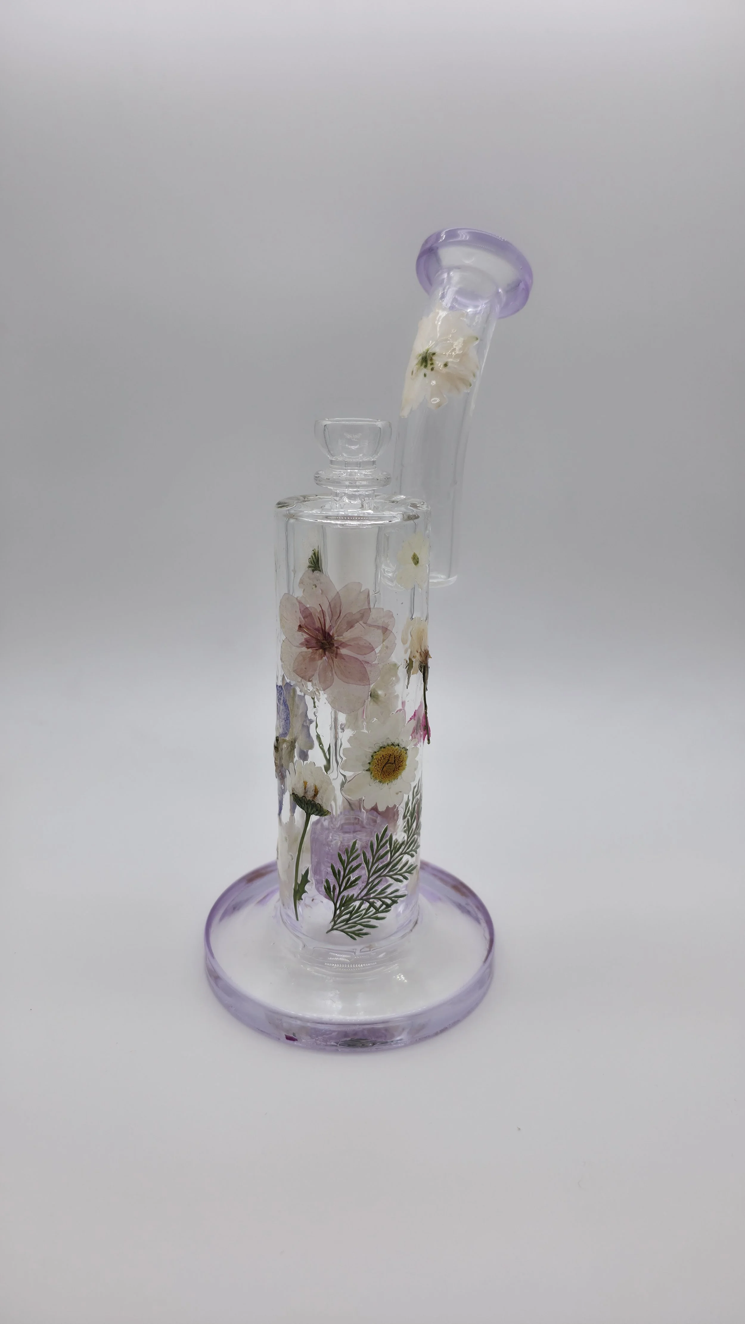 A glass water pipe with floral designs carved into the surface, featuring a purple mouthpiece, on a plain white background.