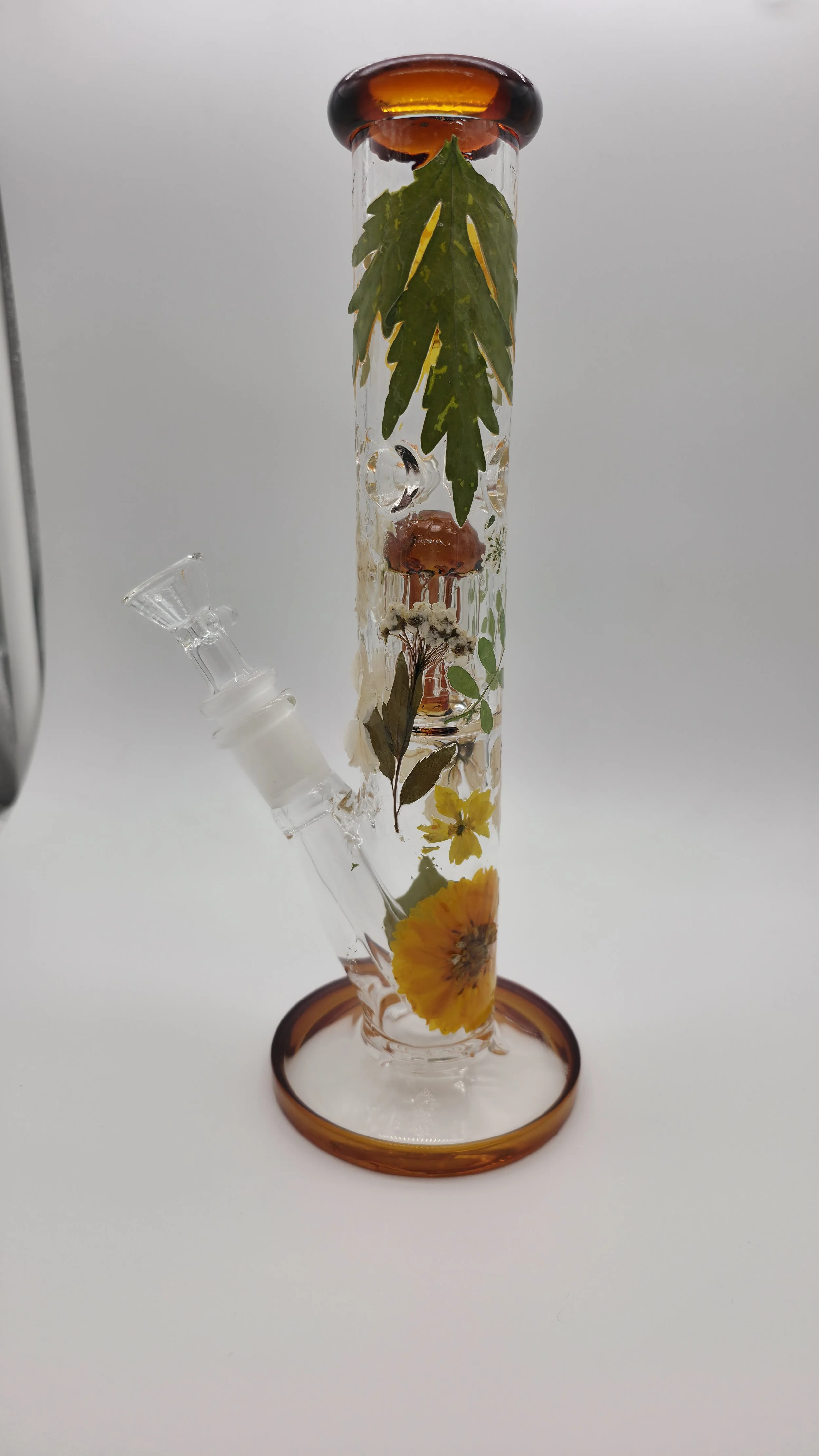 An old glass bong with flowers and leaves inside, placed on a white background.