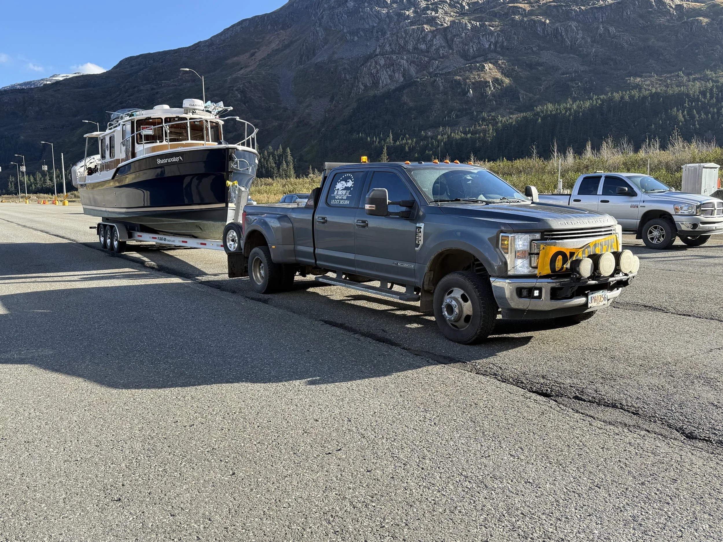 A pickup truck hauling a large boat on a trailer parked on a paved area with mountains in the background.