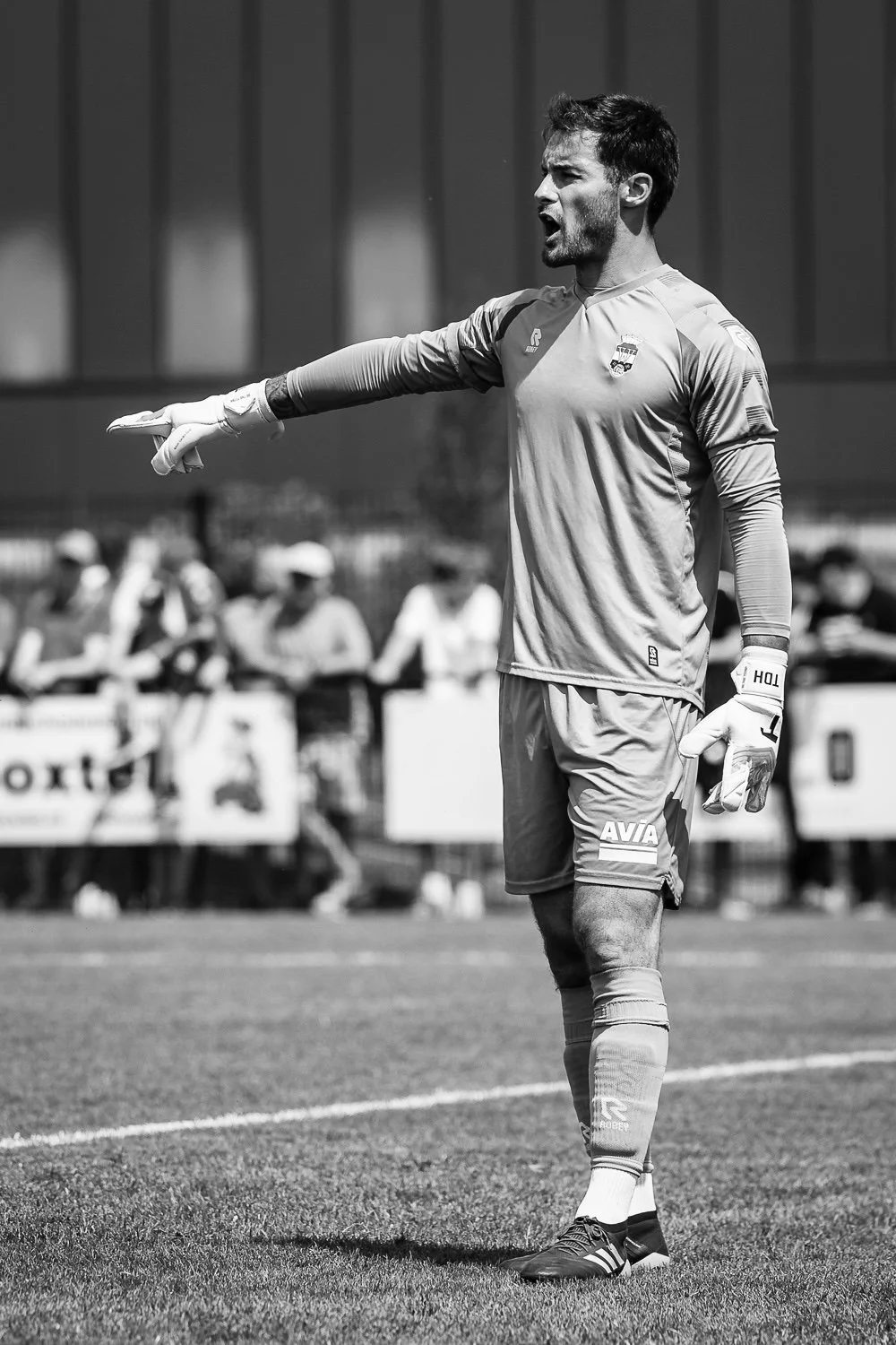 Un gardien de but en uniforme de football avec des gants, pointant du doigt lors d'un match sur un terrain de football.