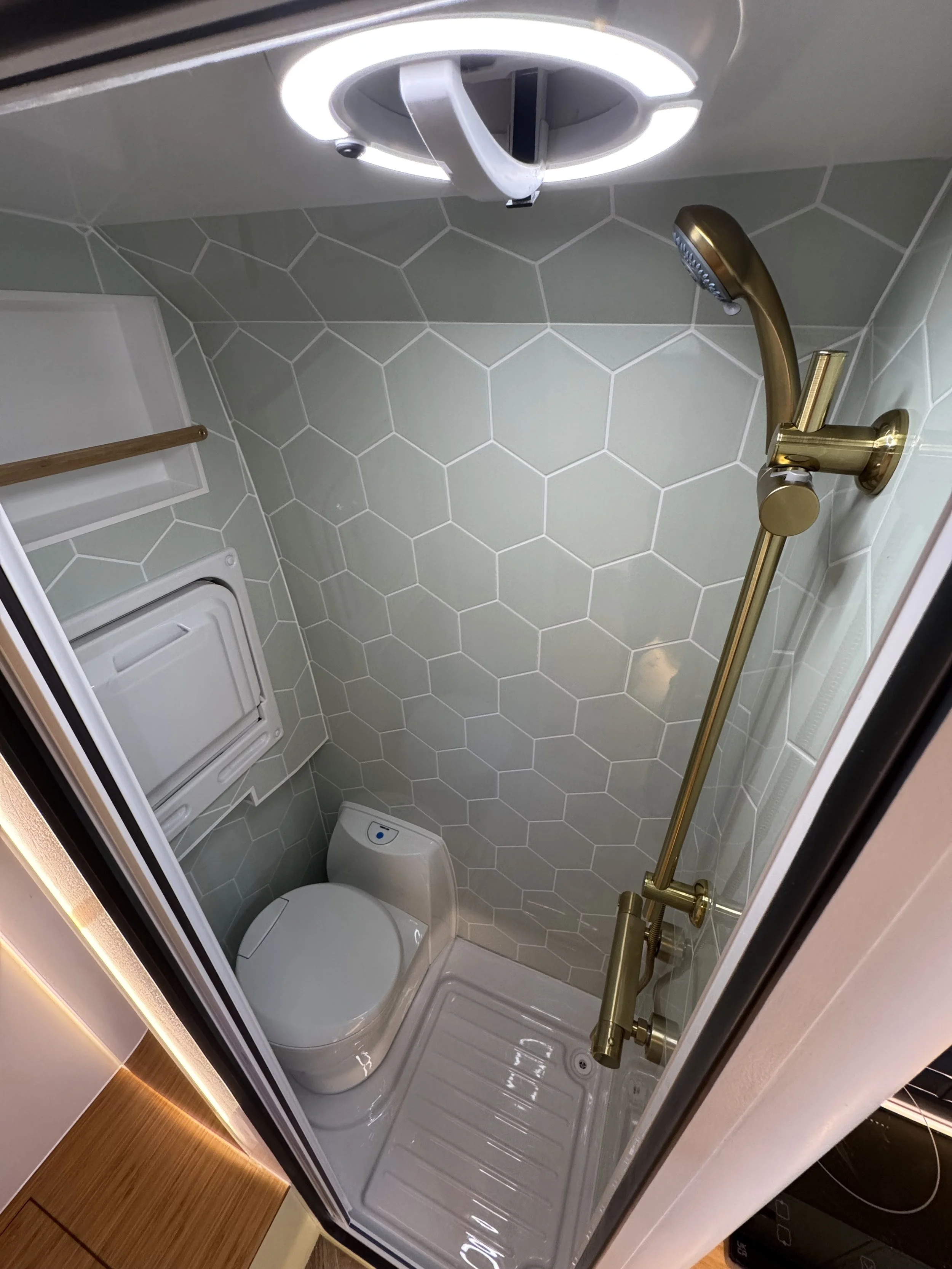 Small bathroom with hexagonal tile walls, a white Toilet, and a golden handheld shower head attached to a corner wall.