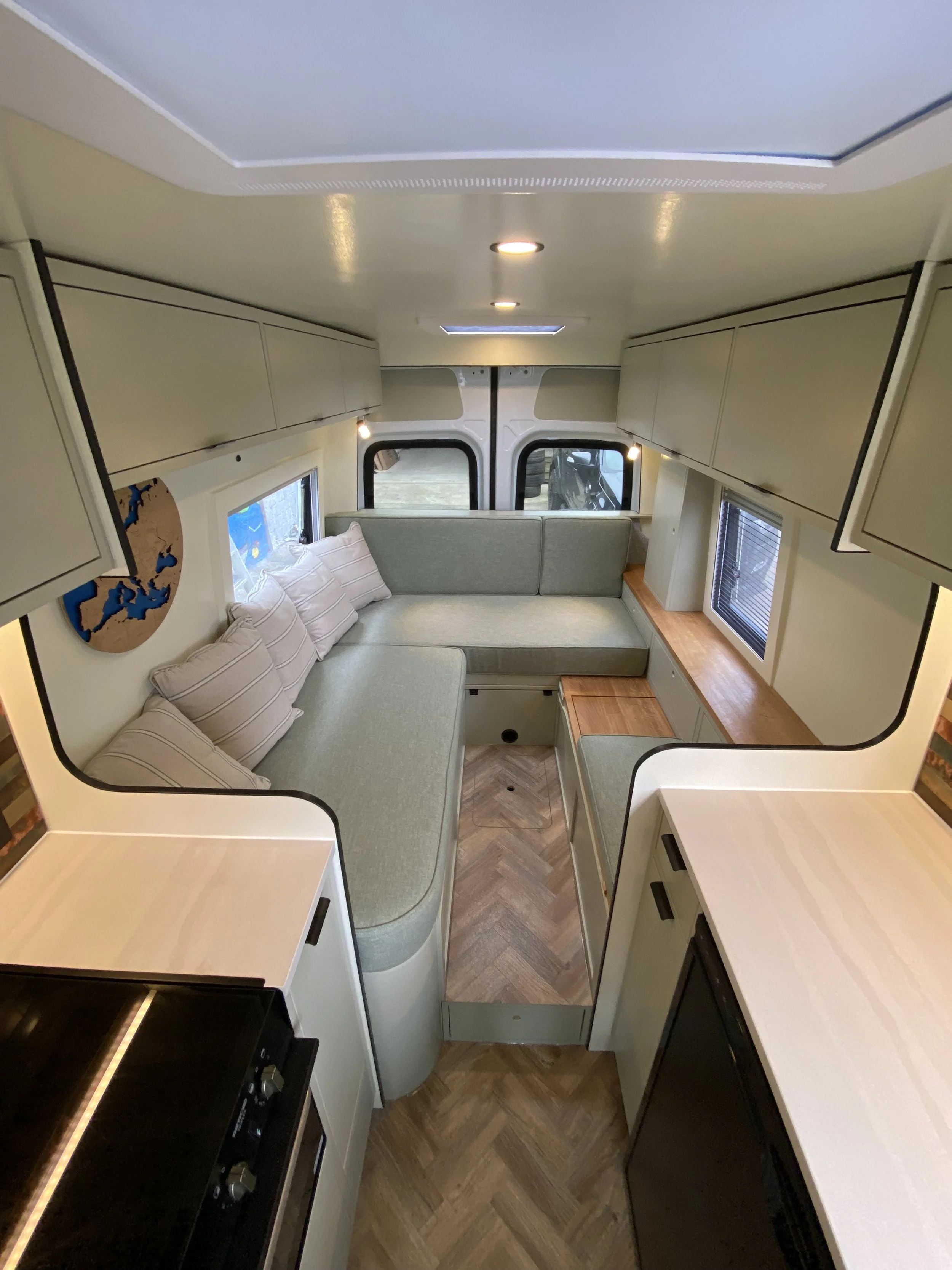 Interior of a small camper or RV with a curved seating area, windows, cabinets, and a wooden floor.