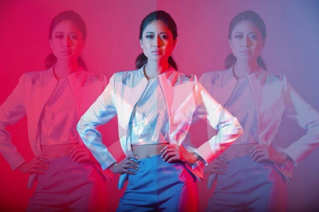 A woman with dark hair tied back, wearing a light-colored jacket and pants, is shown with a layered, semi-transparent effect of three identical images, showing a red and blue color overlay.