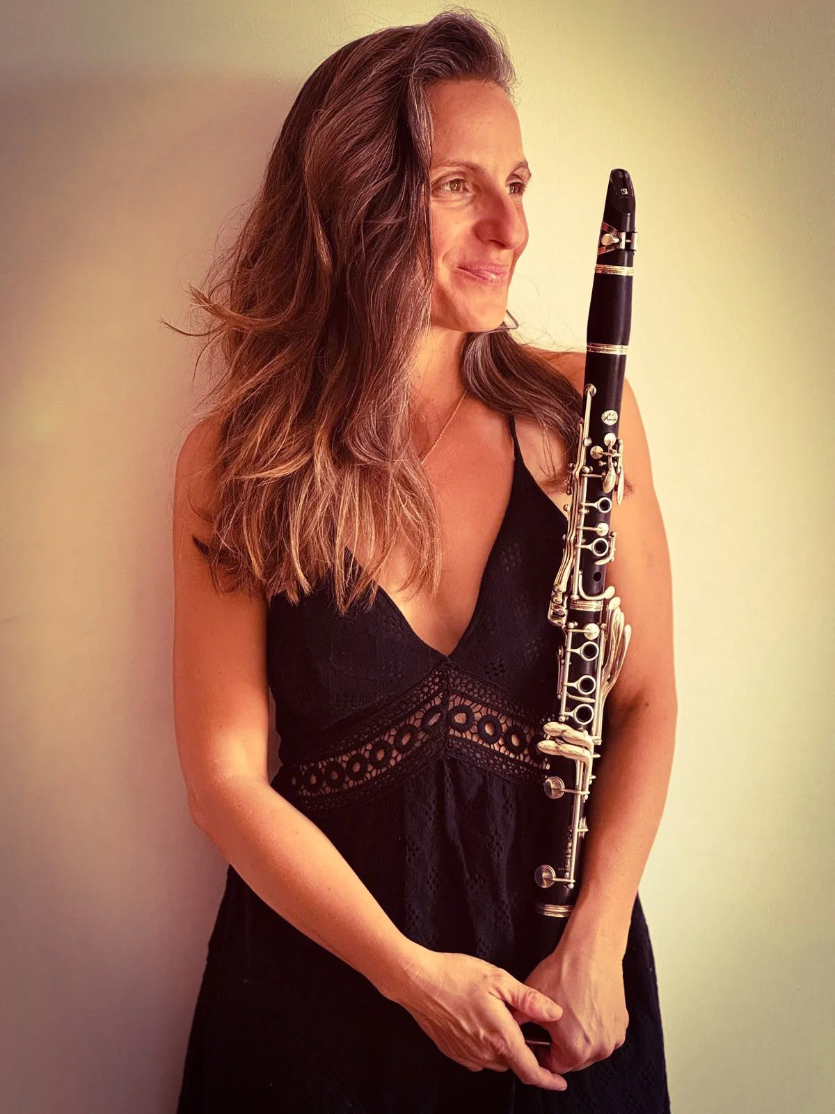 Une femme avec de longs cheveux bruns porte une robe noire en dentelle et tient un hautbois. Elle regarde vers la droite avec un léger sourire.
