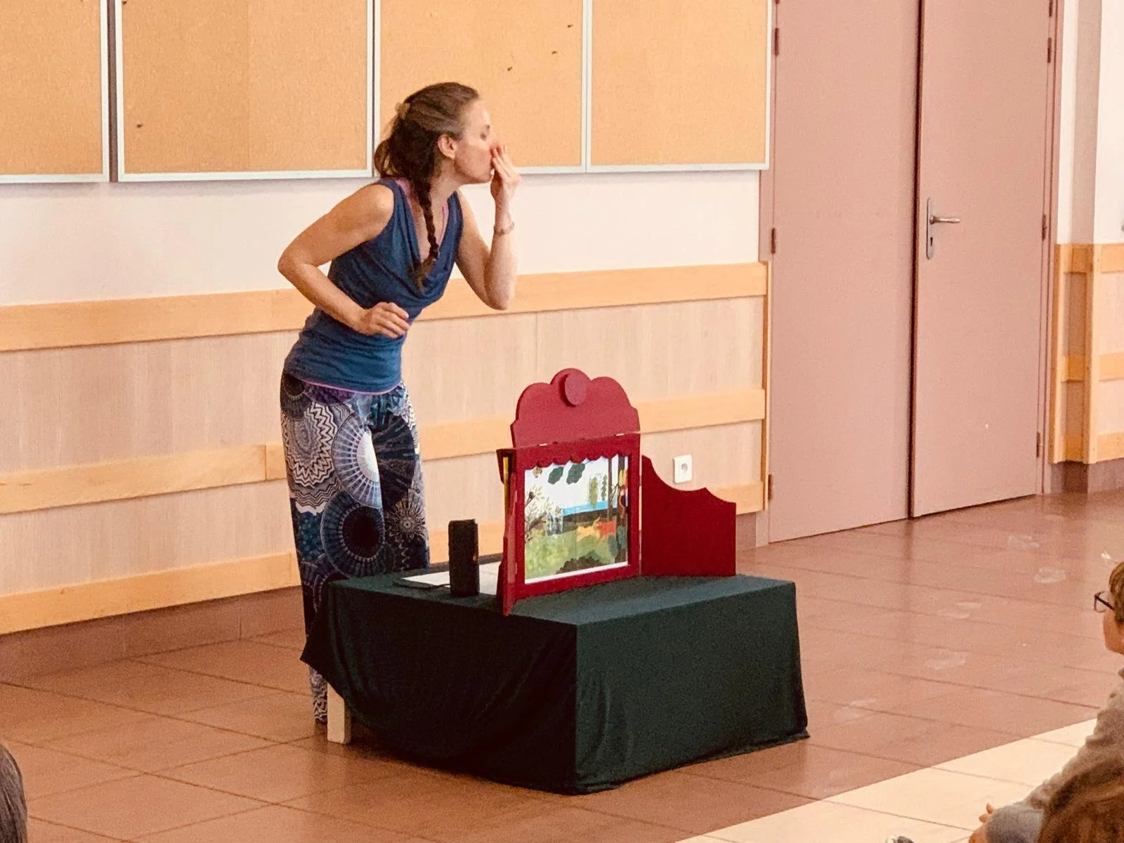 Une femme en train de faire une présentation de théâtre de marionnettes devant un petit public dans une salle.