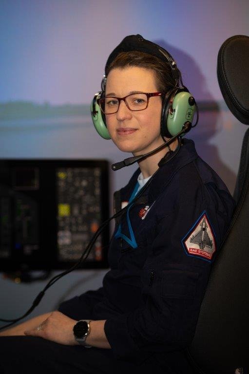 Woman in flying suit wearing pilot headset seated in flight simulator