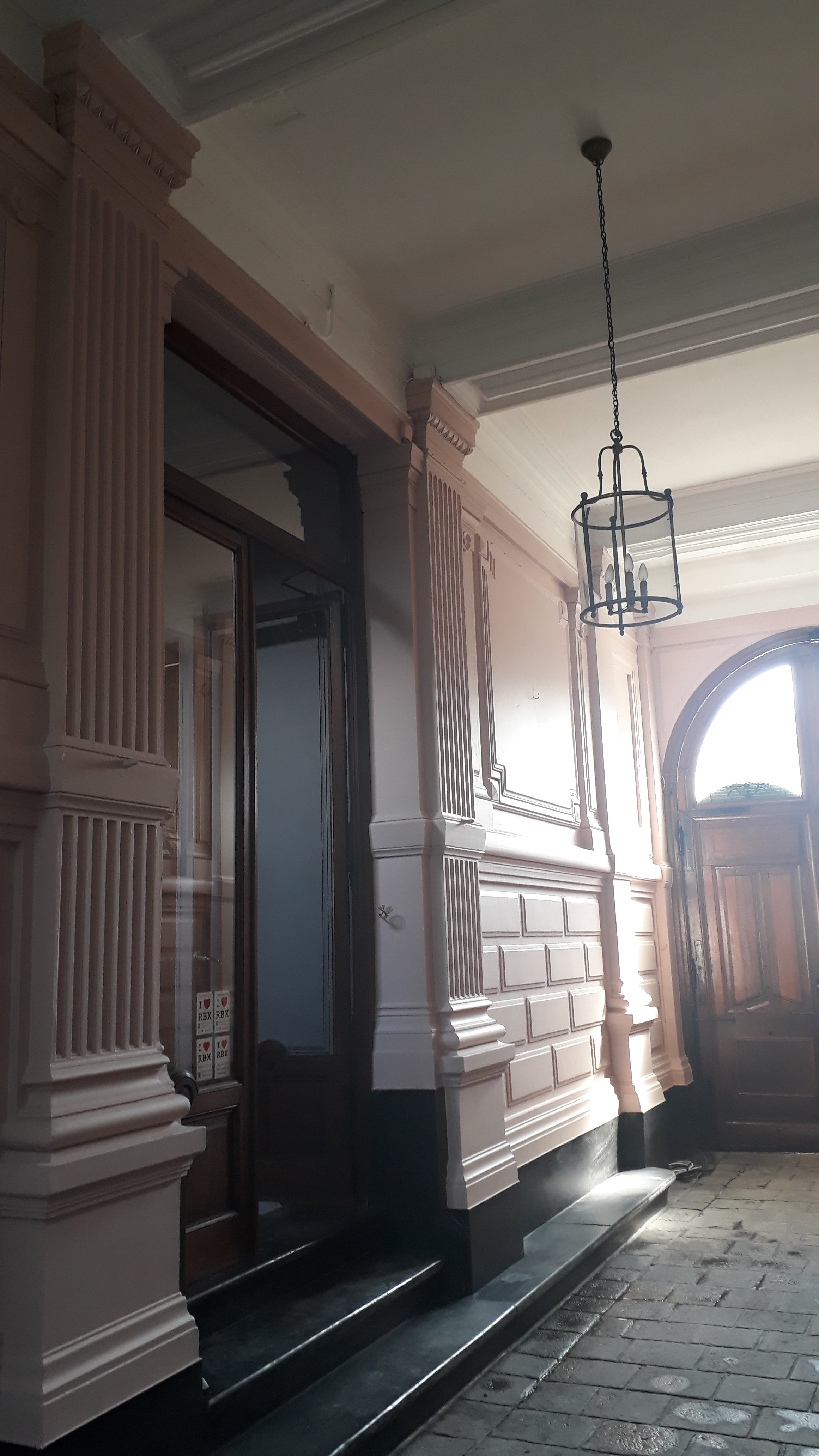 Intérieur avec moulures, chandelier en cage, porte en bois, et fenêtre arquée, sol en pierre.